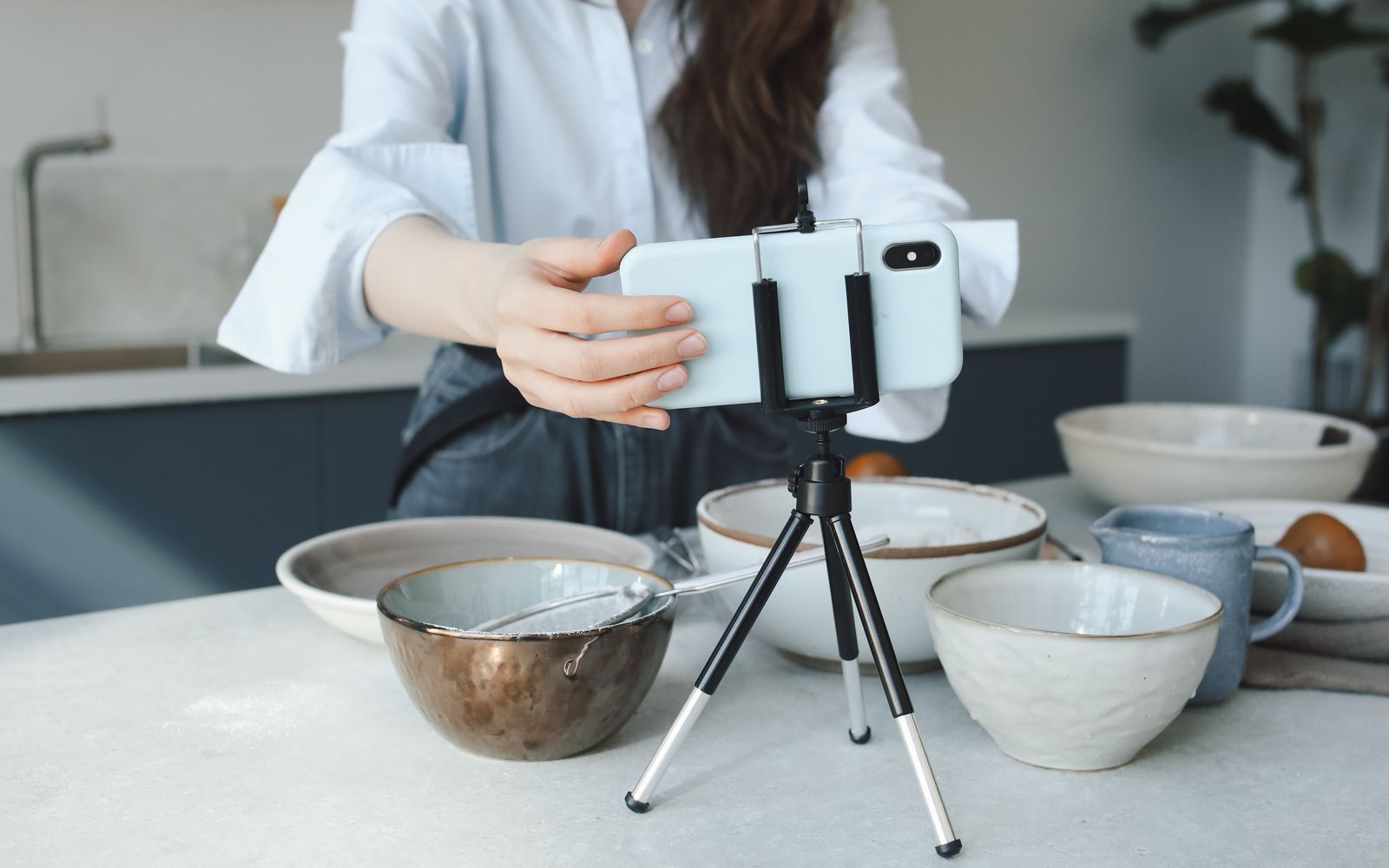 Mulher usando um smartphone em um tripé para vlog na cozinha com tigelas