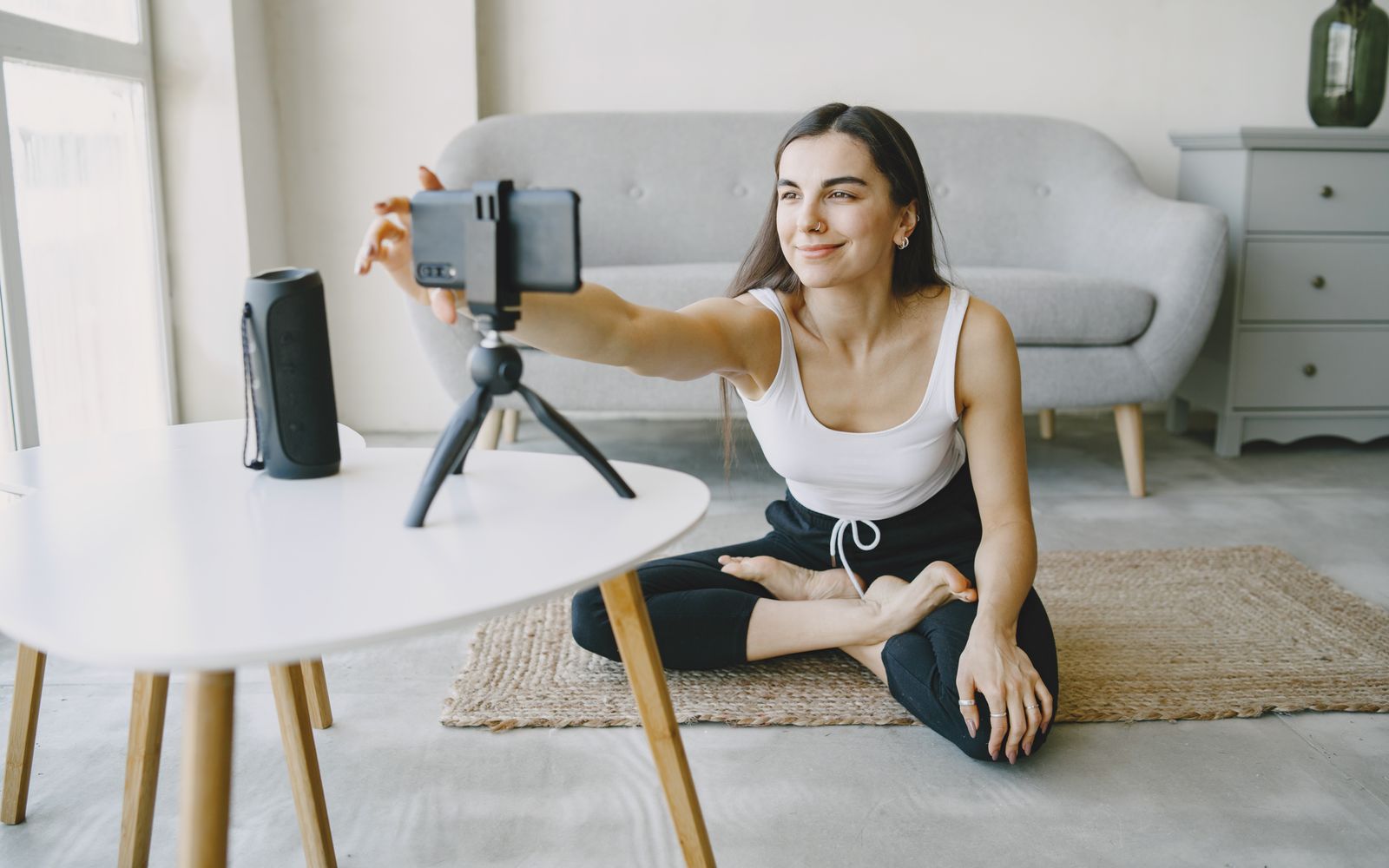 Mulher sorrindo usando um top vlogando dentro de casa usando um smartphone e um tripé