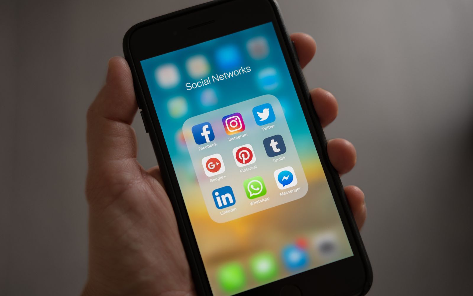 Mão segurando celular com vários ícones de redes sociais