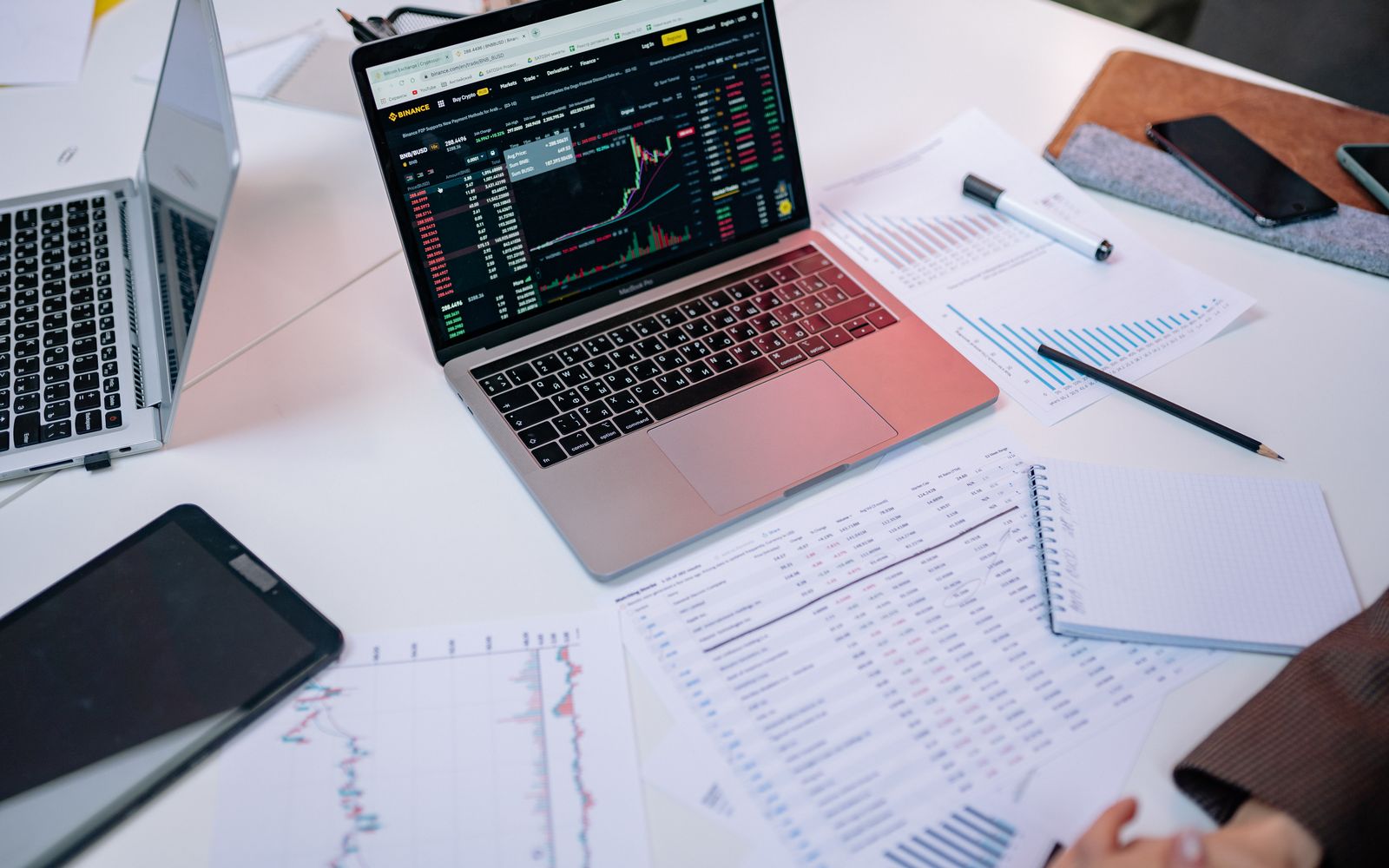 Notebooks em uma mesa exibindo gráficos de bolsa de valores e documentos financeiros