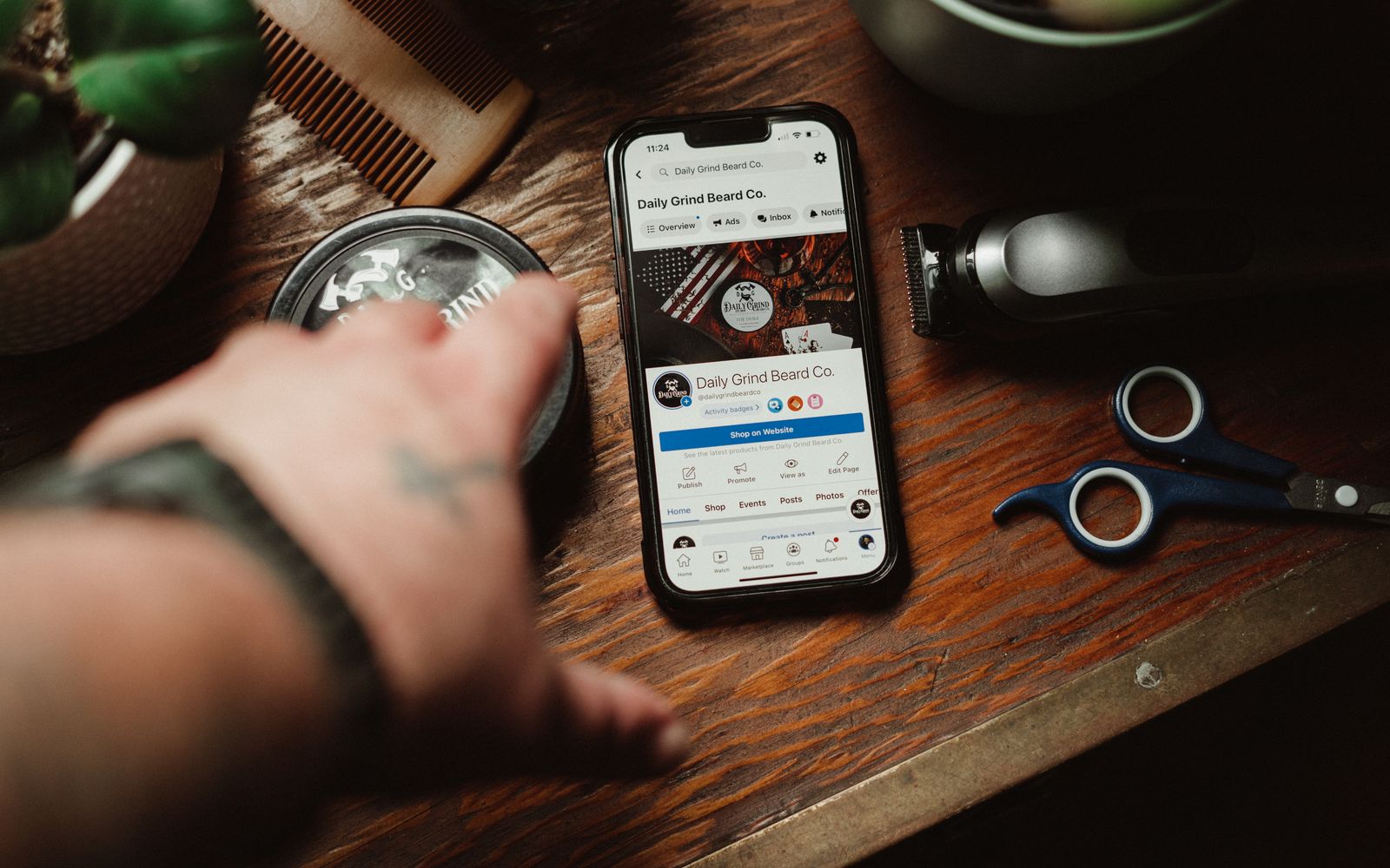 Ferramentas de barbeiro e um smartphone exibindo o site de uma marca de cuidados pessoais sobre uma mesa de madeira