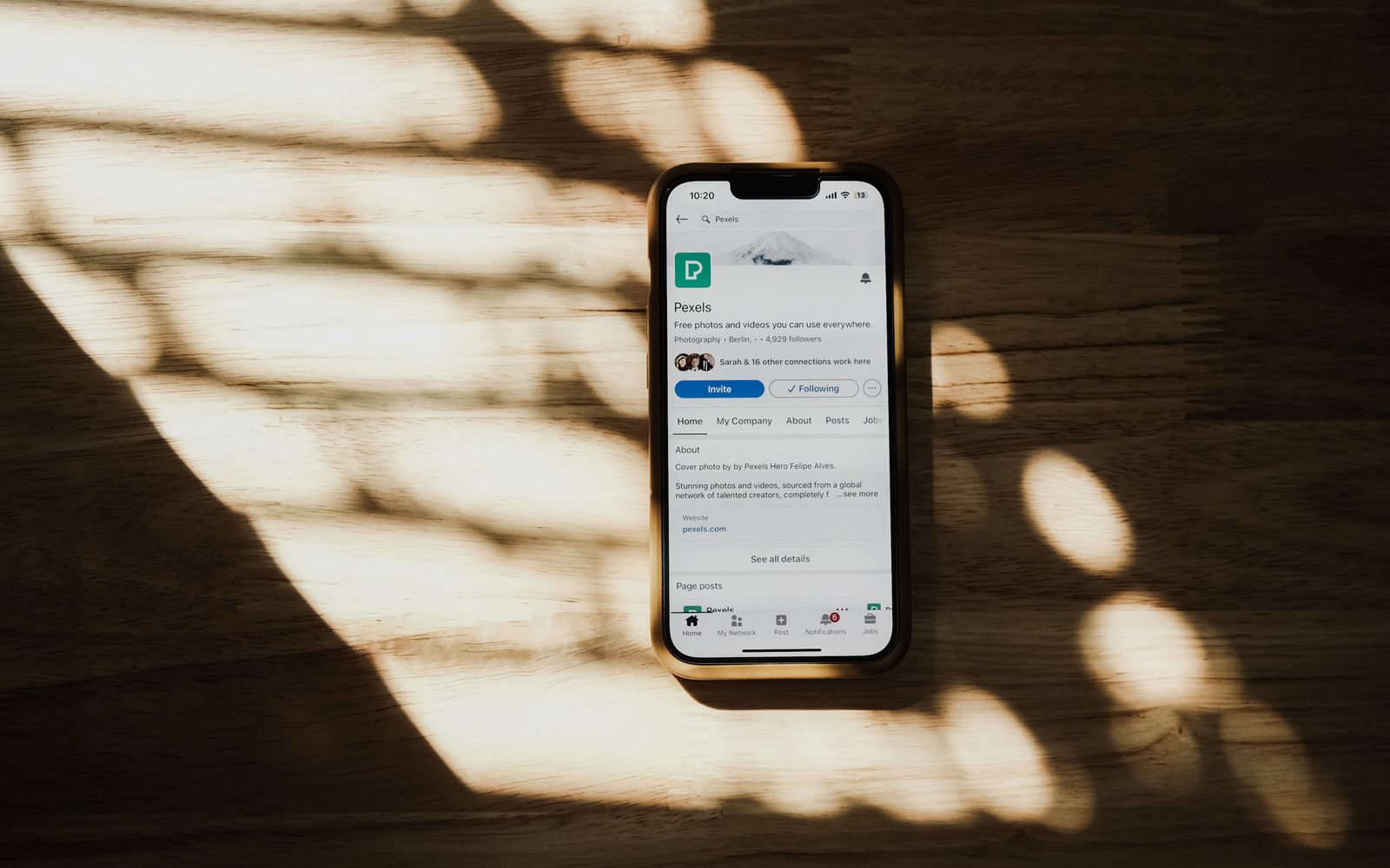 Um smartphone exibindo um perfil de rede social sobre uma mesa de madeira iluminada pelo sol
