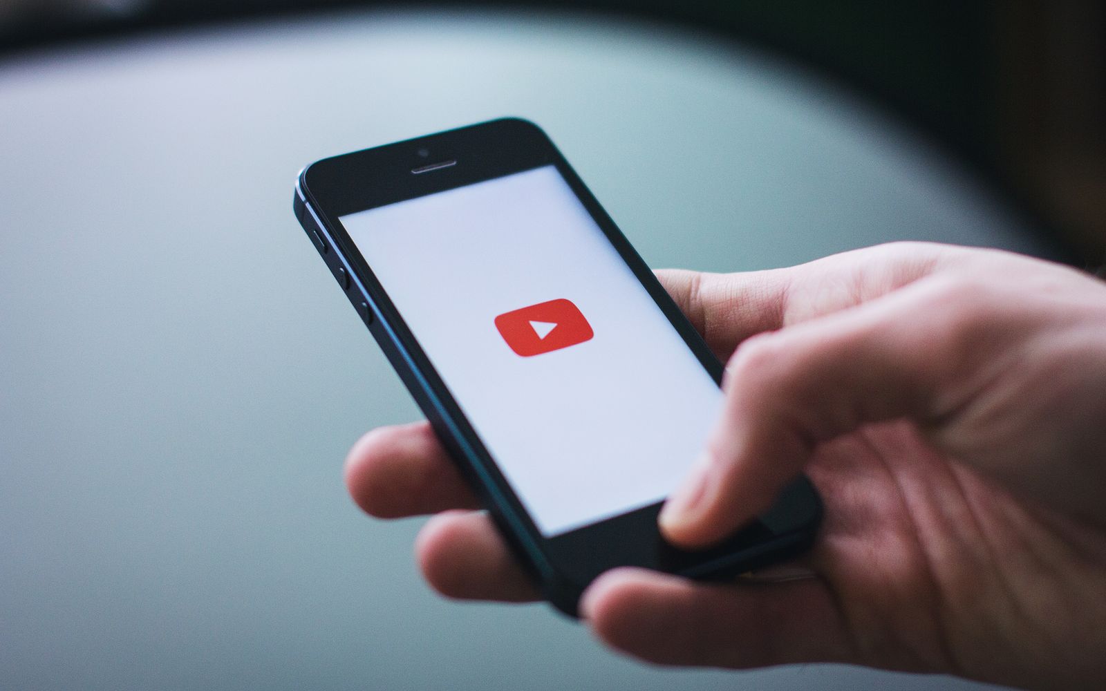 Foto em close de uma mão segurando um smartphone com a tela exibindo o aplicativo YouTube