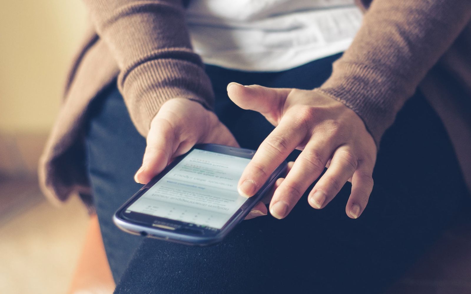 Foto em close de um adulto usando smartphone em ambiente interno, navegando na web com foco na tela