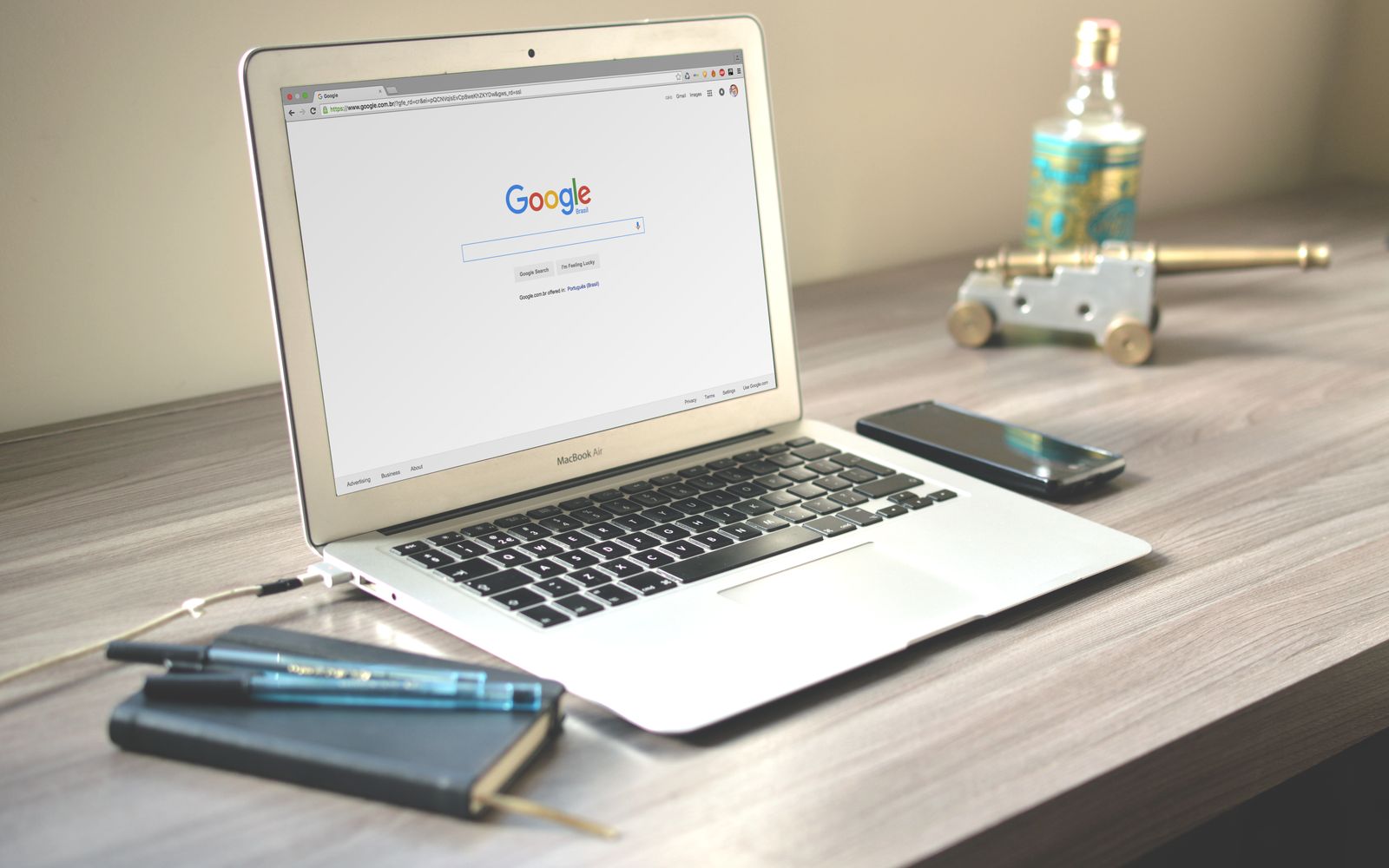 Mesa de madeira com notebook aberto na busca do Google, celular e caderno