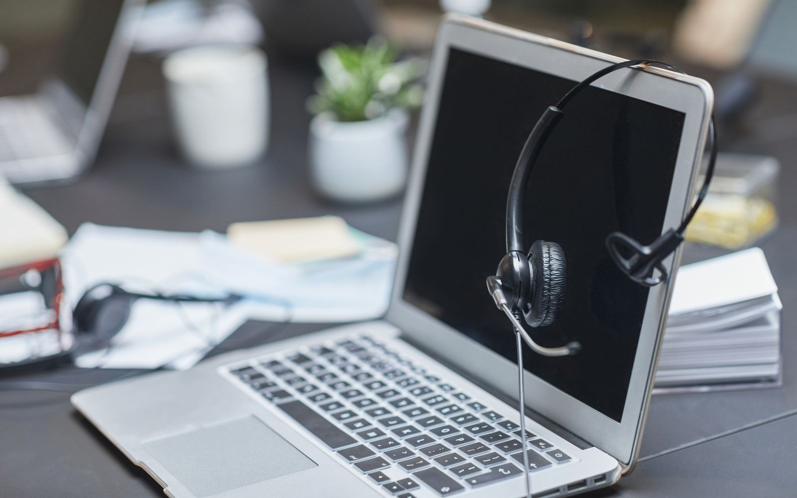 Um fone de ouvido colocado em um laptop em um ambiente de escritório moderno e bagunçado com papéis e plantas