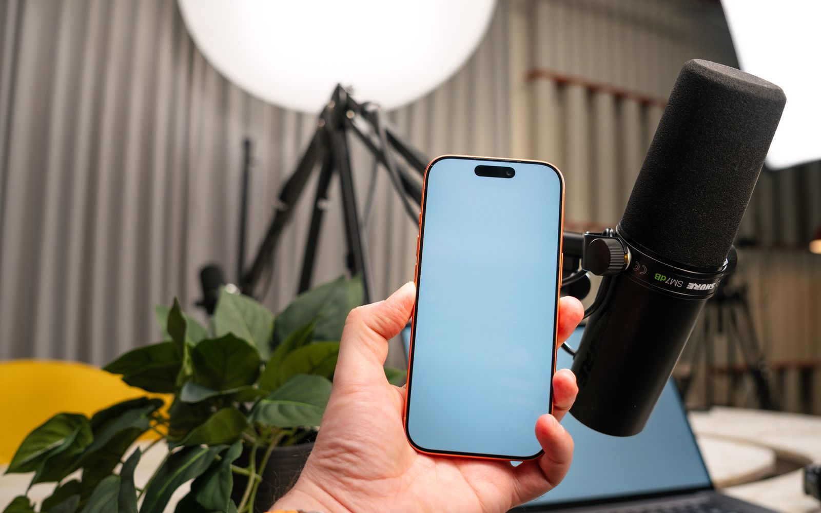Configuração de estúdio de podcast com uma mão segurando um smartphone e um microfone profissional para gravação