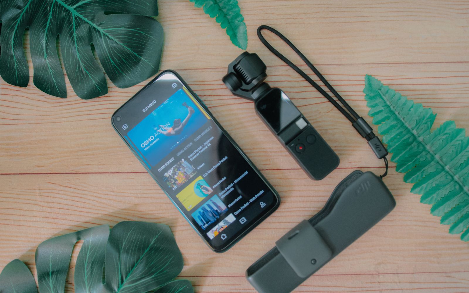 Composição vista de cima com smartphone mostrando foto subaquática na tela, colocado perto de uma câmera de ação portátil e um pendrive sobre uma mesa de madeira com folhas de plantas tropicais