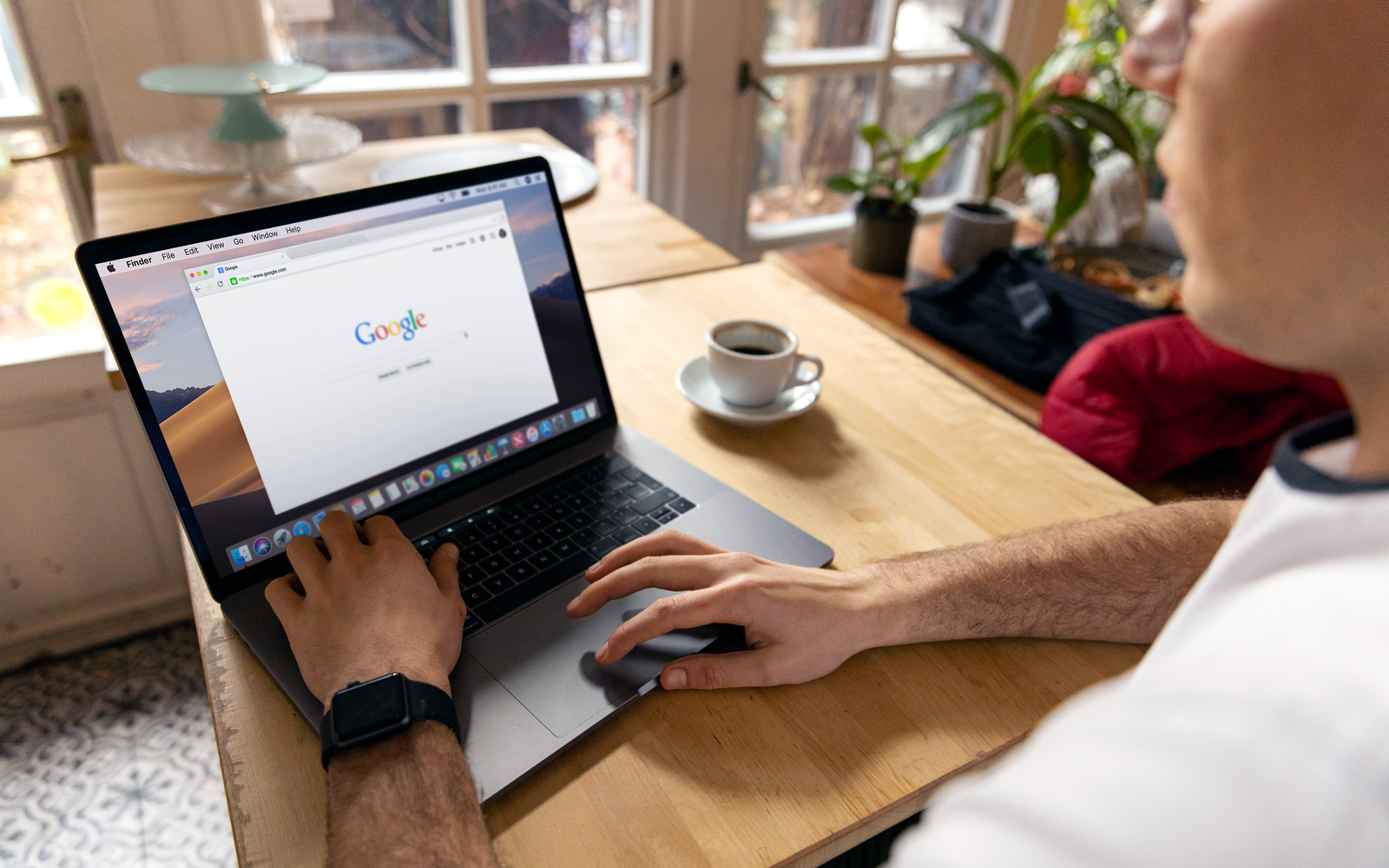 Pessoa navegando na internet pelo notebook, com um café na mesa de madeira