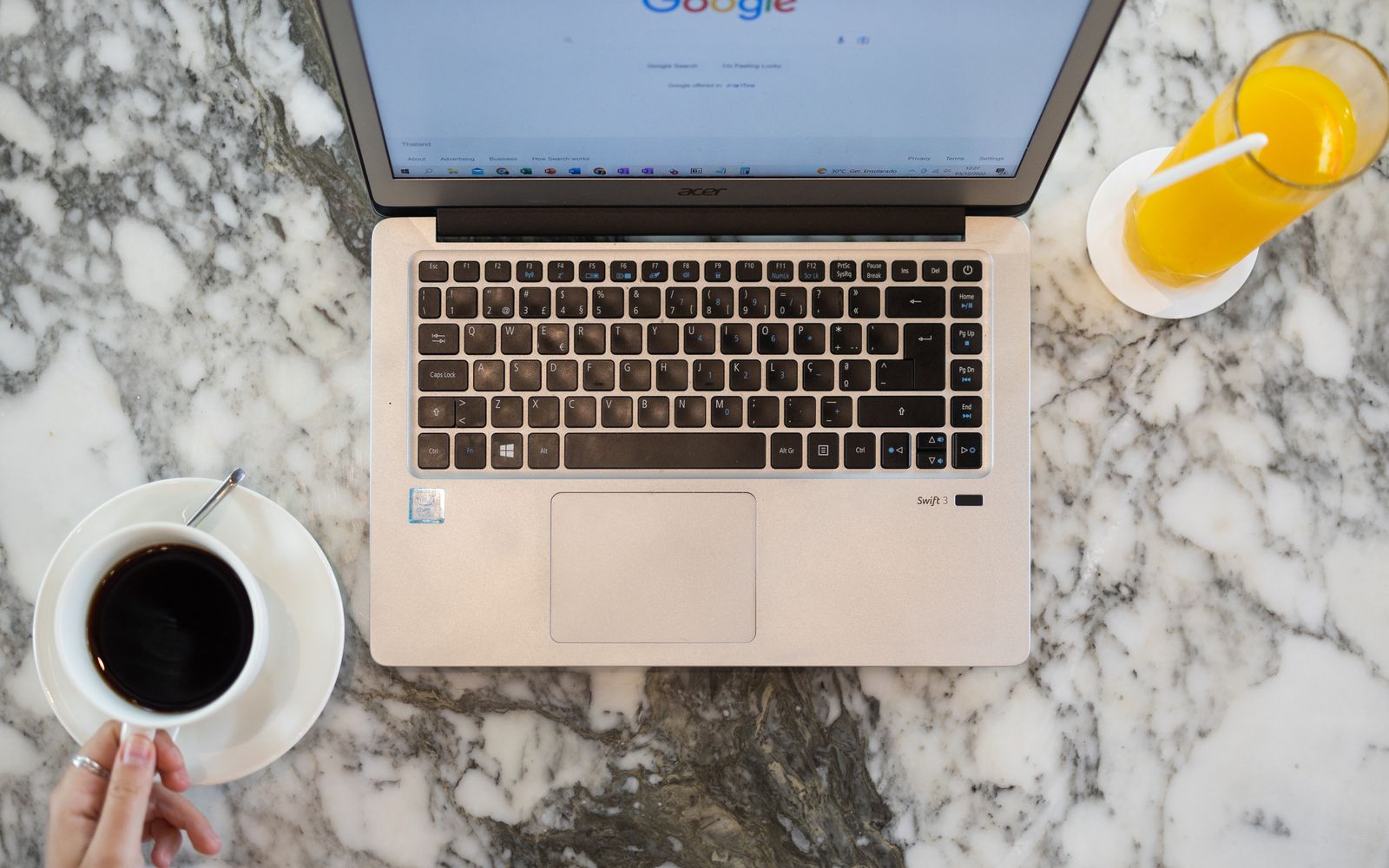 Mesa de mármore vista de cima com notebook, café e suco de laranja