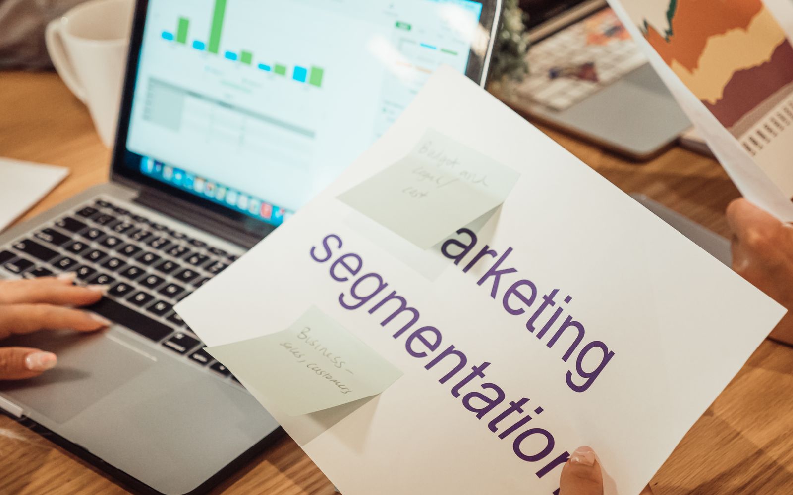 Mãos analisando dados de marketing no notebook e em documentos impressos