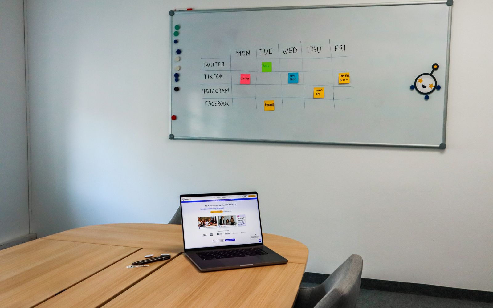 Configuração de escritório com mesa de reunião, laptop e quadro-branco organizado com horários