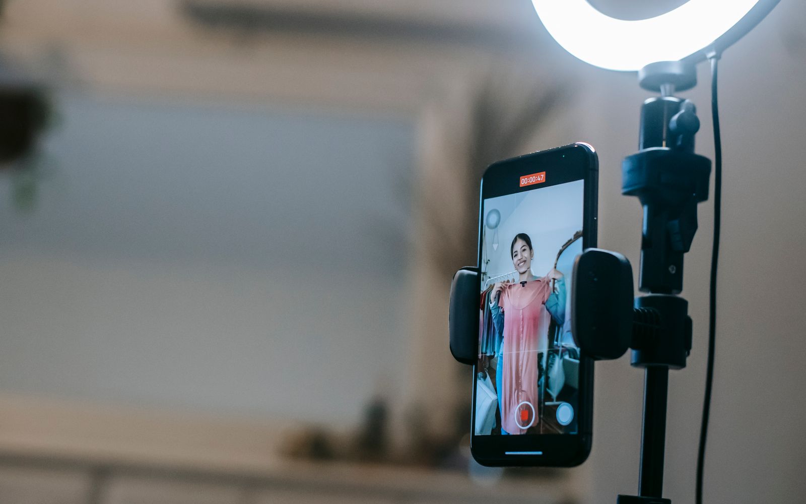 Criadora gravando vídeo no celular com luz de anel, mostrando um vestido rosa