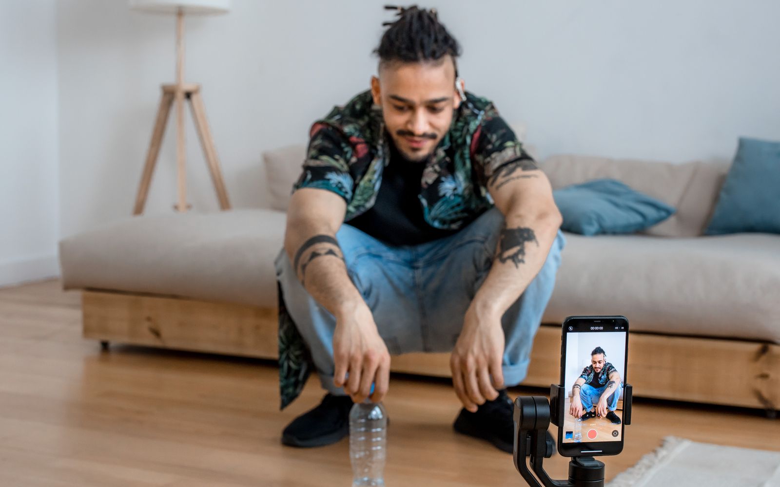Jovem gravando conteúdo na sala com o celular em tripé
