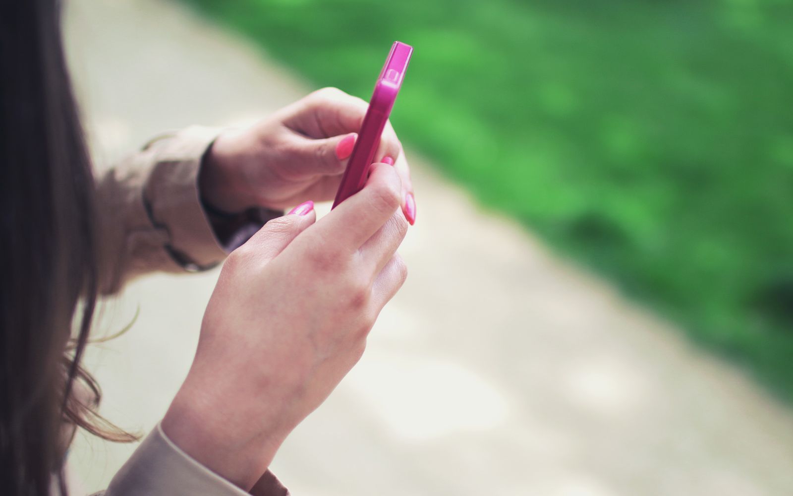 Mulher segurando um celular rosa com as duas mãos ao ar livre