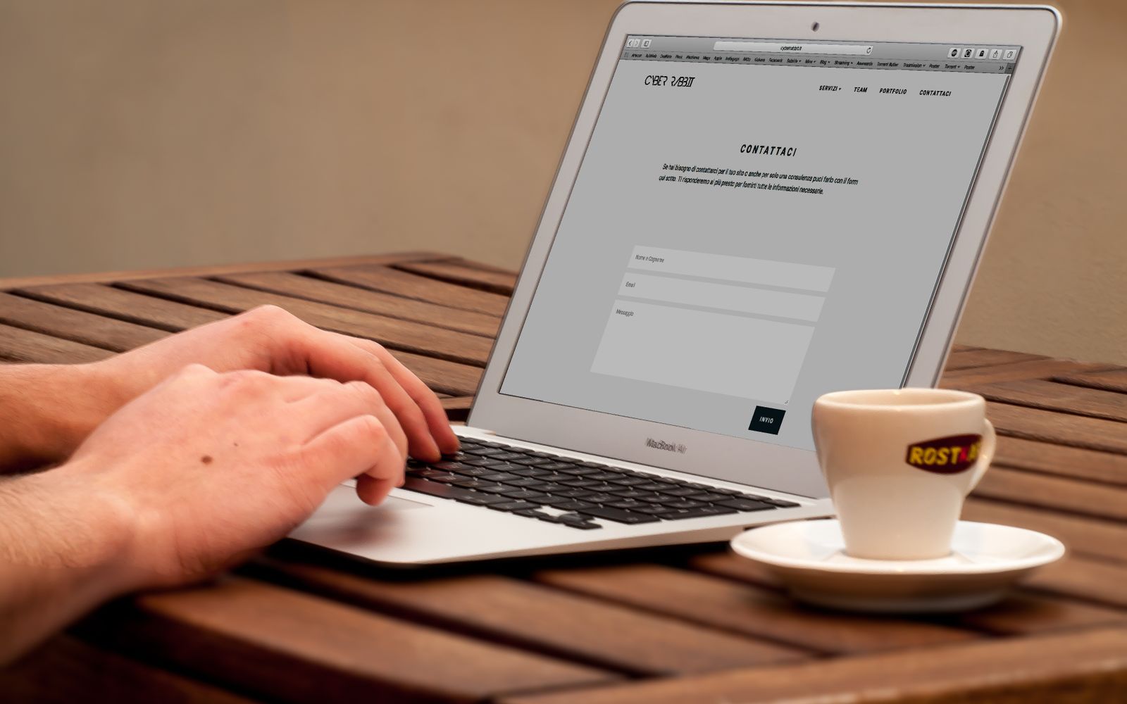 Mãos digitando em um laptop ao lado de uma xícara de café em uma mesa de madeira