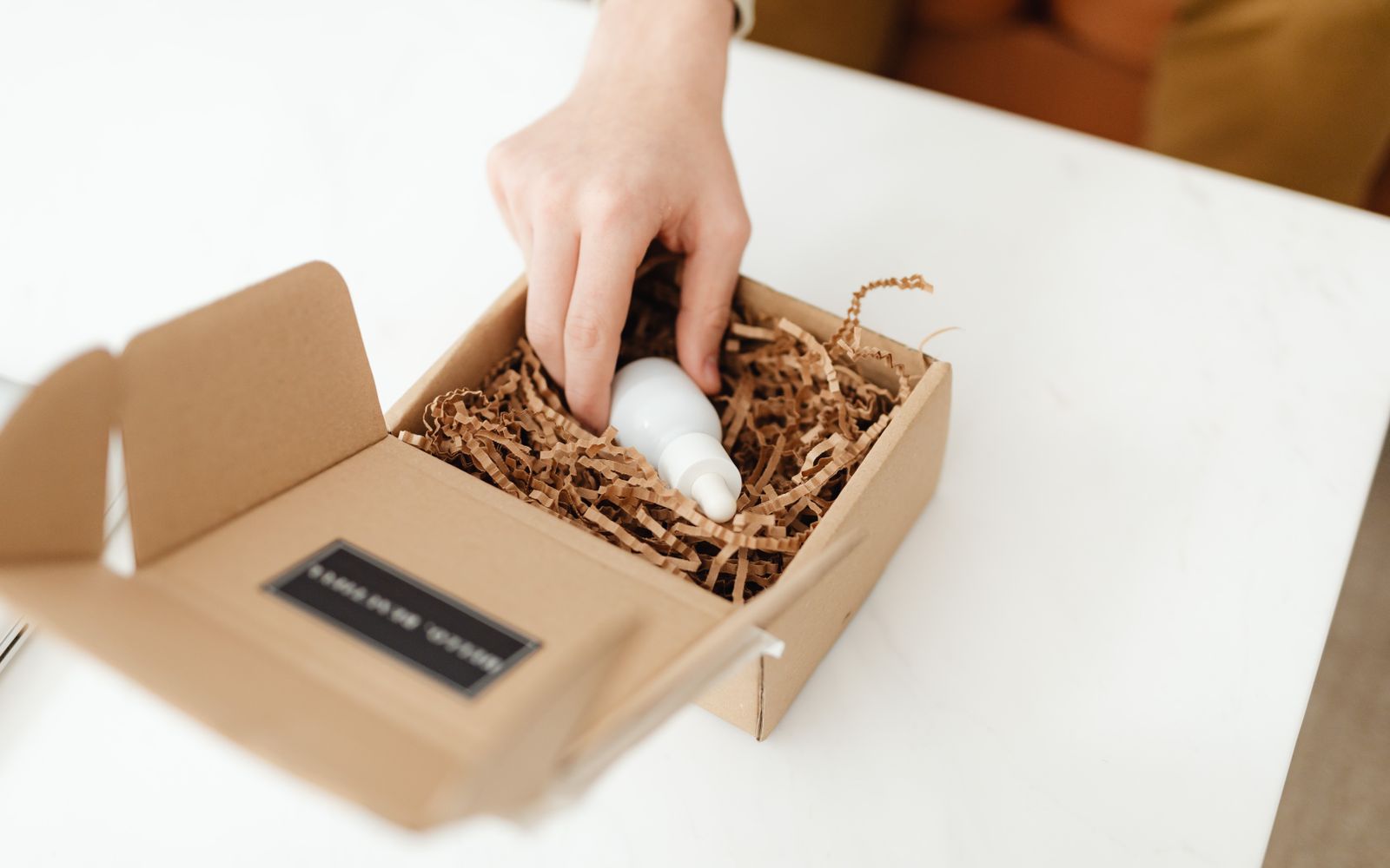 Mão abrindo uma caixa de papelão com um frasco de produto dentro