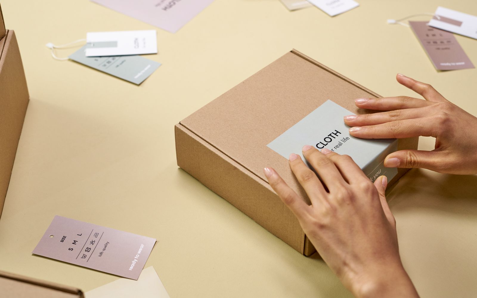 Mãos embalando uma caixa de papelão cercada de etiquetas