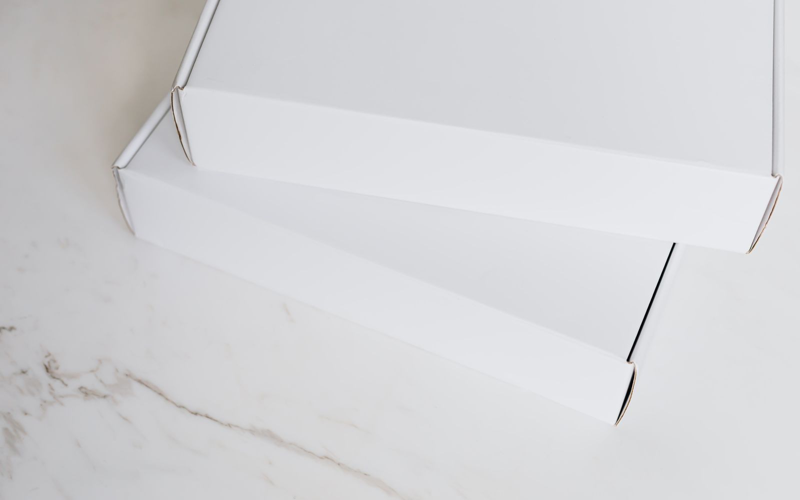 Duas caixas brancas fechadas, prontas para envio, sobre mesa de mármore