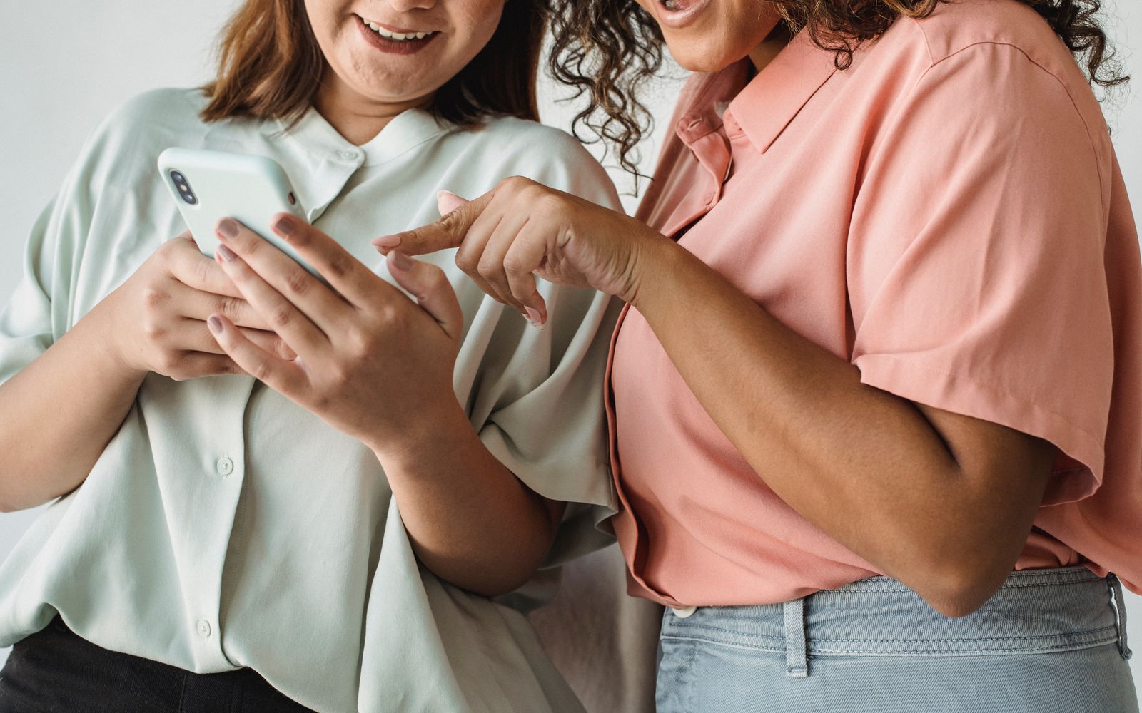 Foto em close de duas mulheres interagindo com um smartphone, sorrindo e se envolvendo com a tecnologia