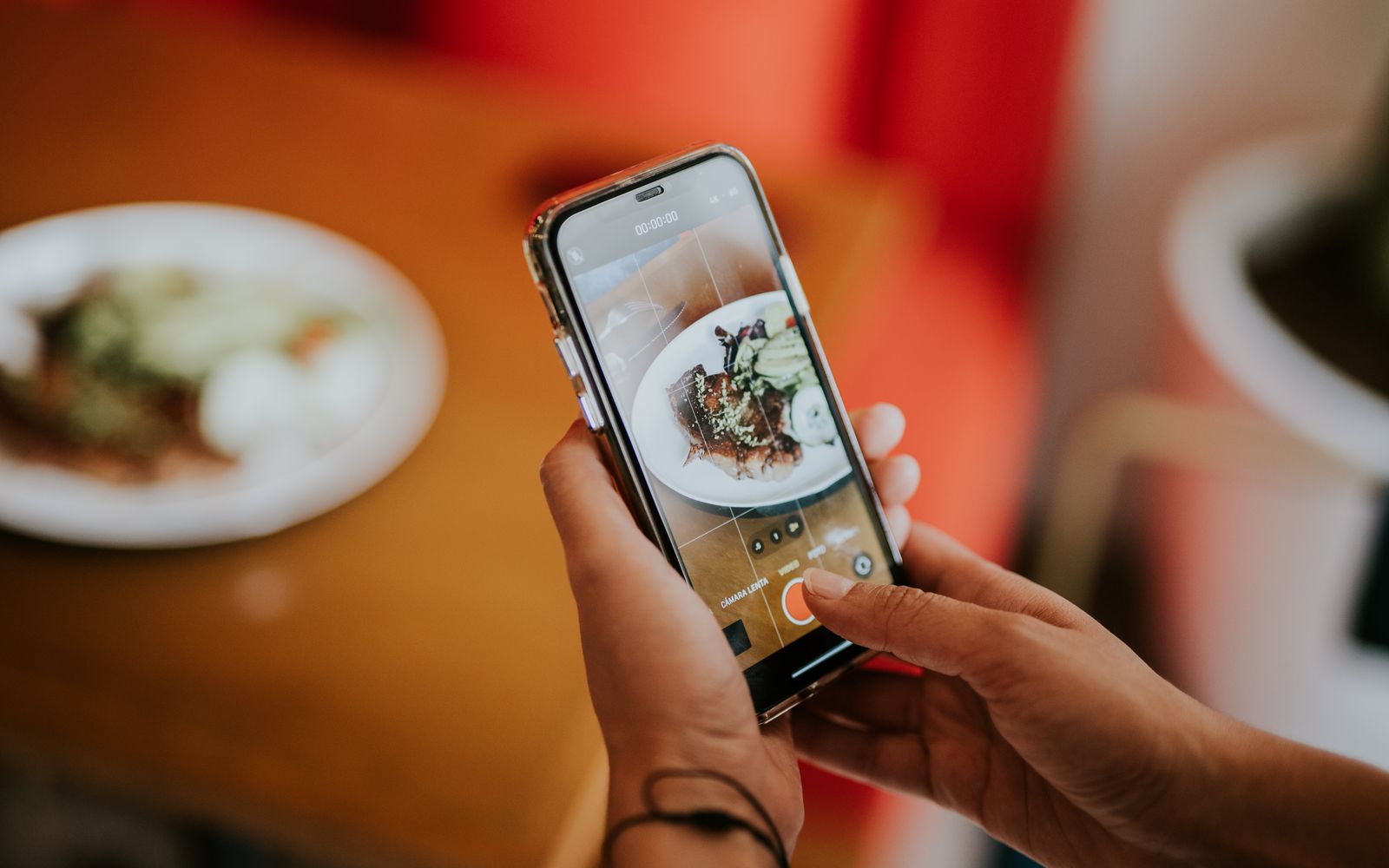Foto em close de uma pessoa usando um smartphone para tirar uma foto de comida em um ambiente interno acolhedor