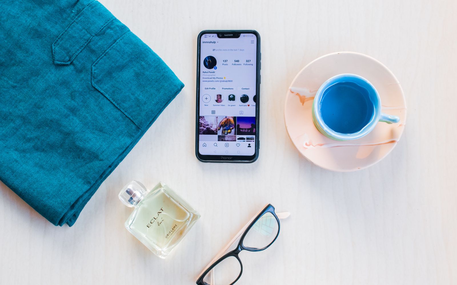 Celular moderno visto de cima com imagens na tela próximo a uma xícara de bebida colorida e um frasco de perfume