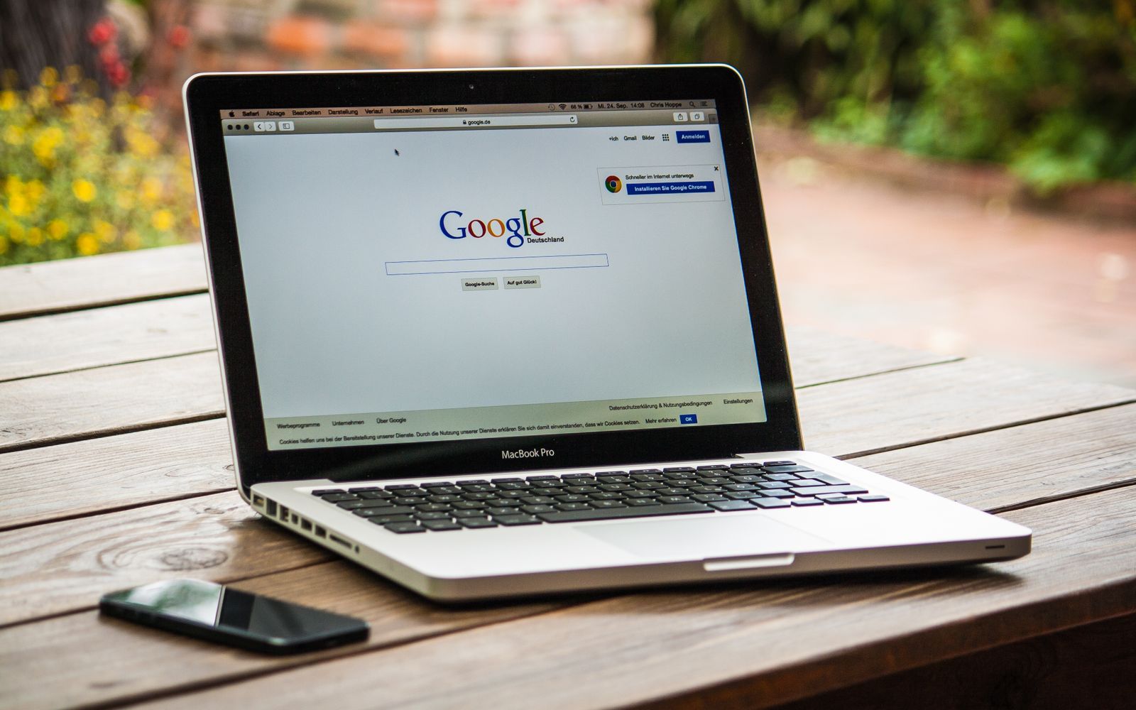 MacBook Pro com a busca do Google aberta em mesa ao ar livre, ao lado de um celular