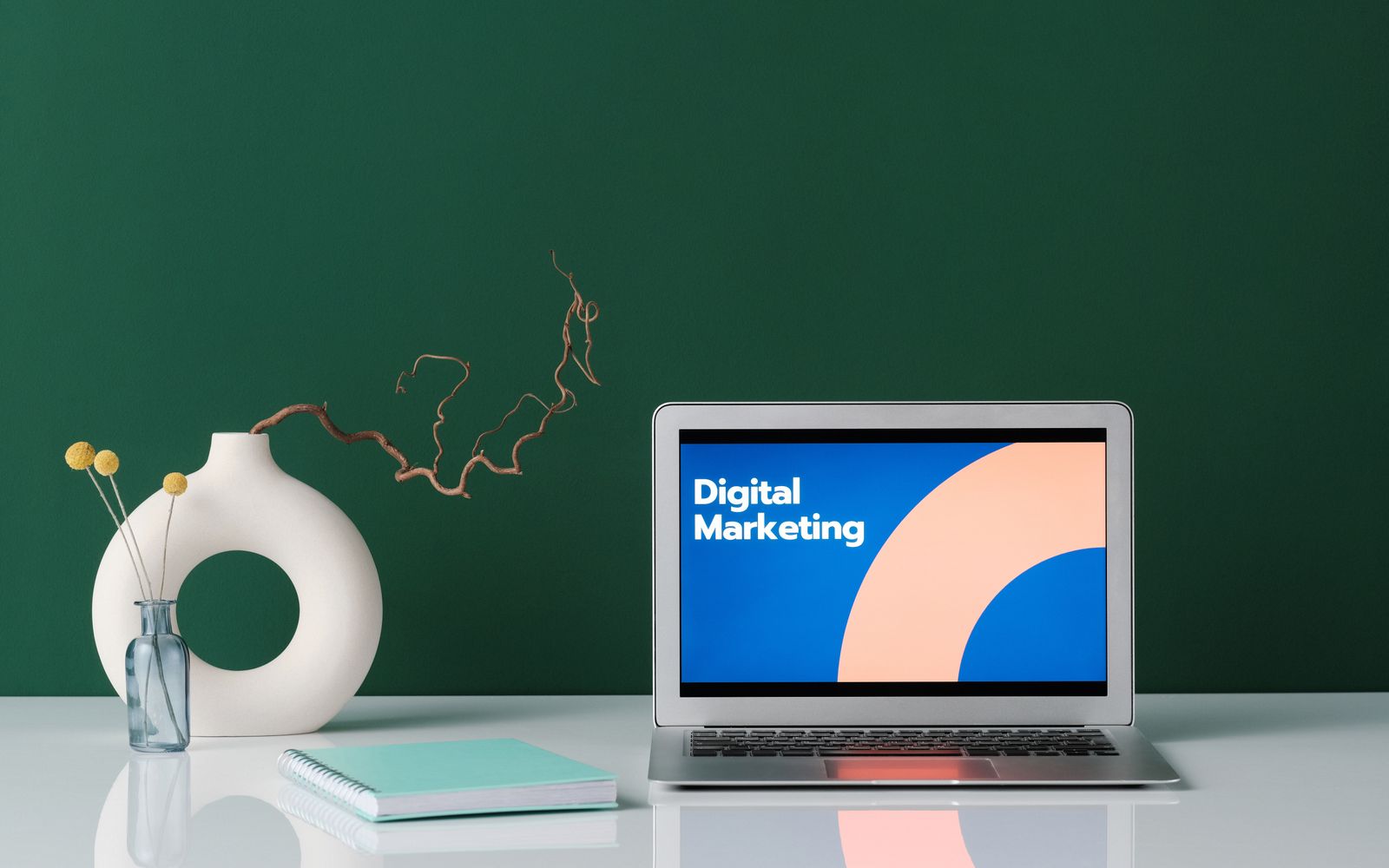 Notebook exibindo a expressão Digital Marketing diante de uma parede verde