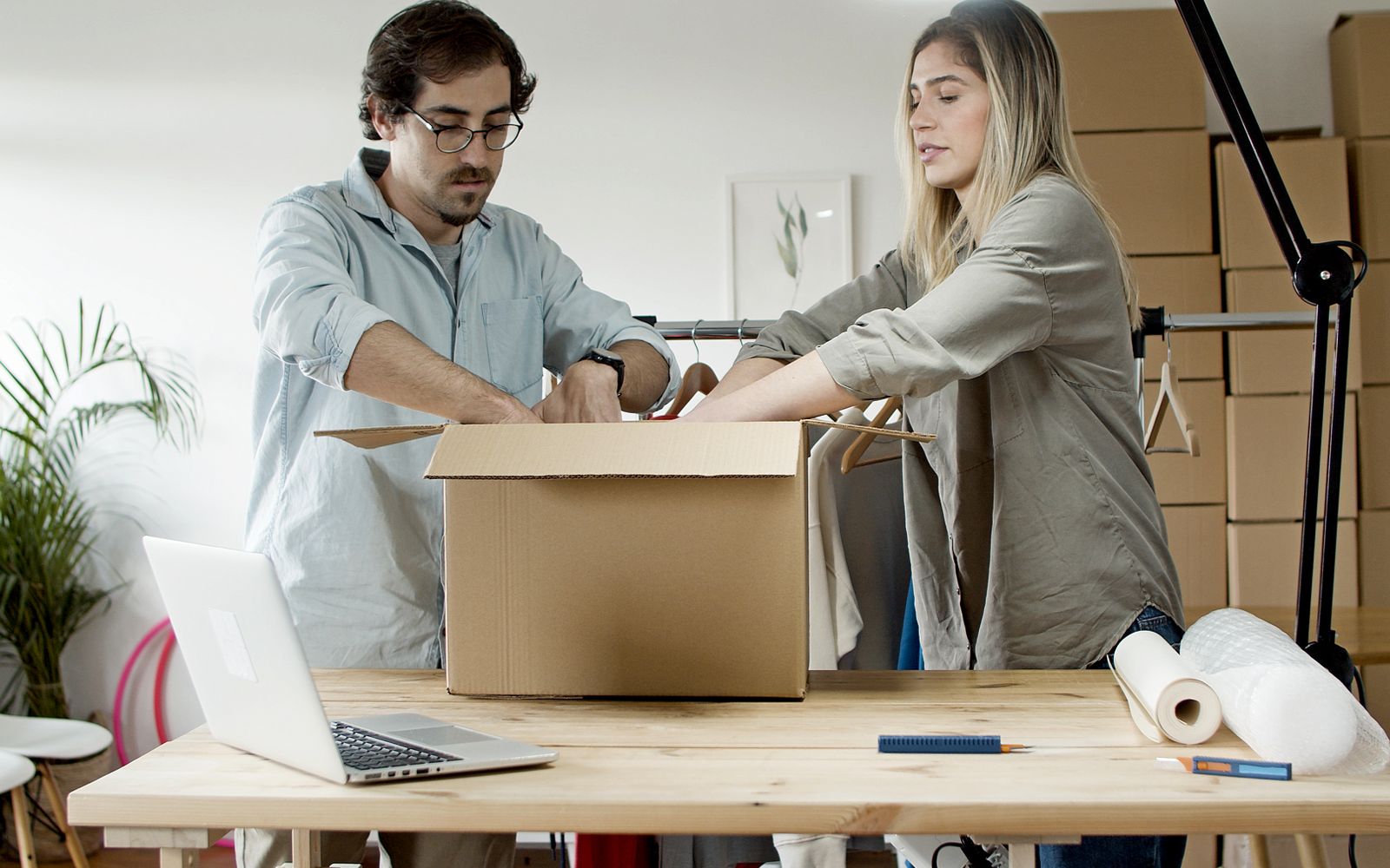 Homem e mulher embalando pedidos de e-commerce com notebook e caixas