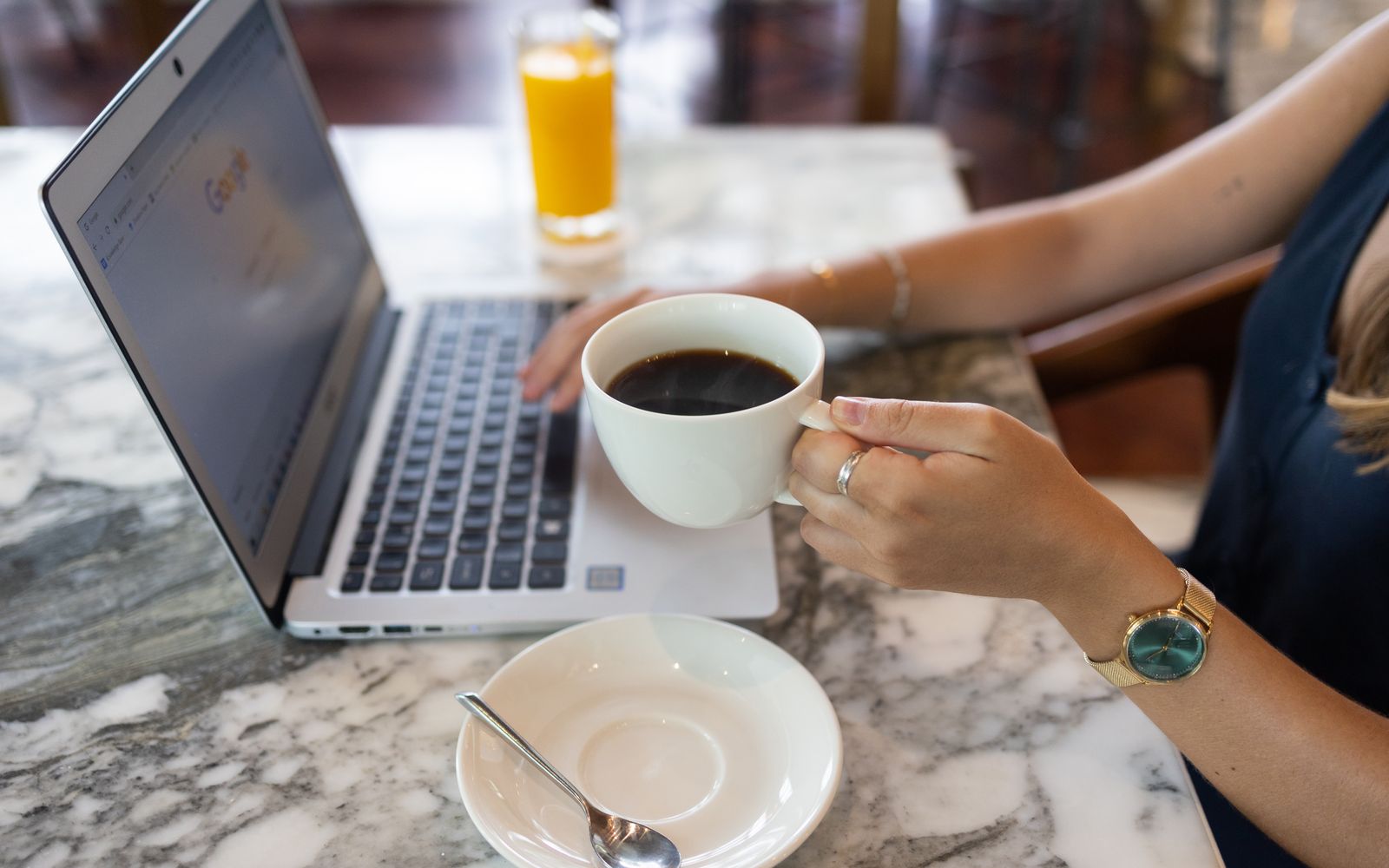 Mulher trabalhando no notebook em um café, com uma xícara na mão