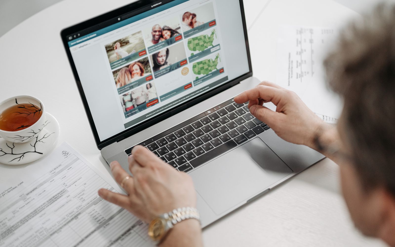 Pessoa navegando em um site pelo notebook, com xícara de chá e documentos