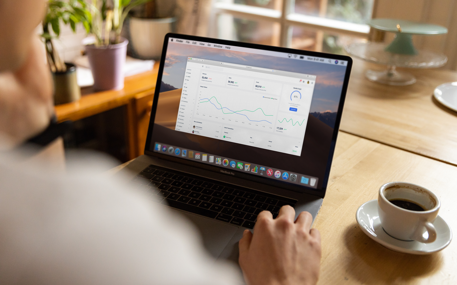 Pessoa analisando dados do mercado de ações em laptop dentro de casa, em ambiente casual, com café