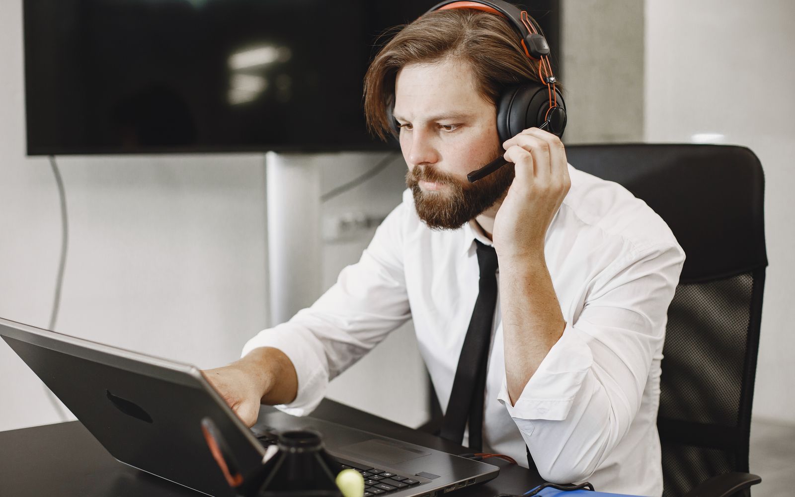 Homem concentrado usando laptop e fone de ouvido, vestindo roupa de escritório