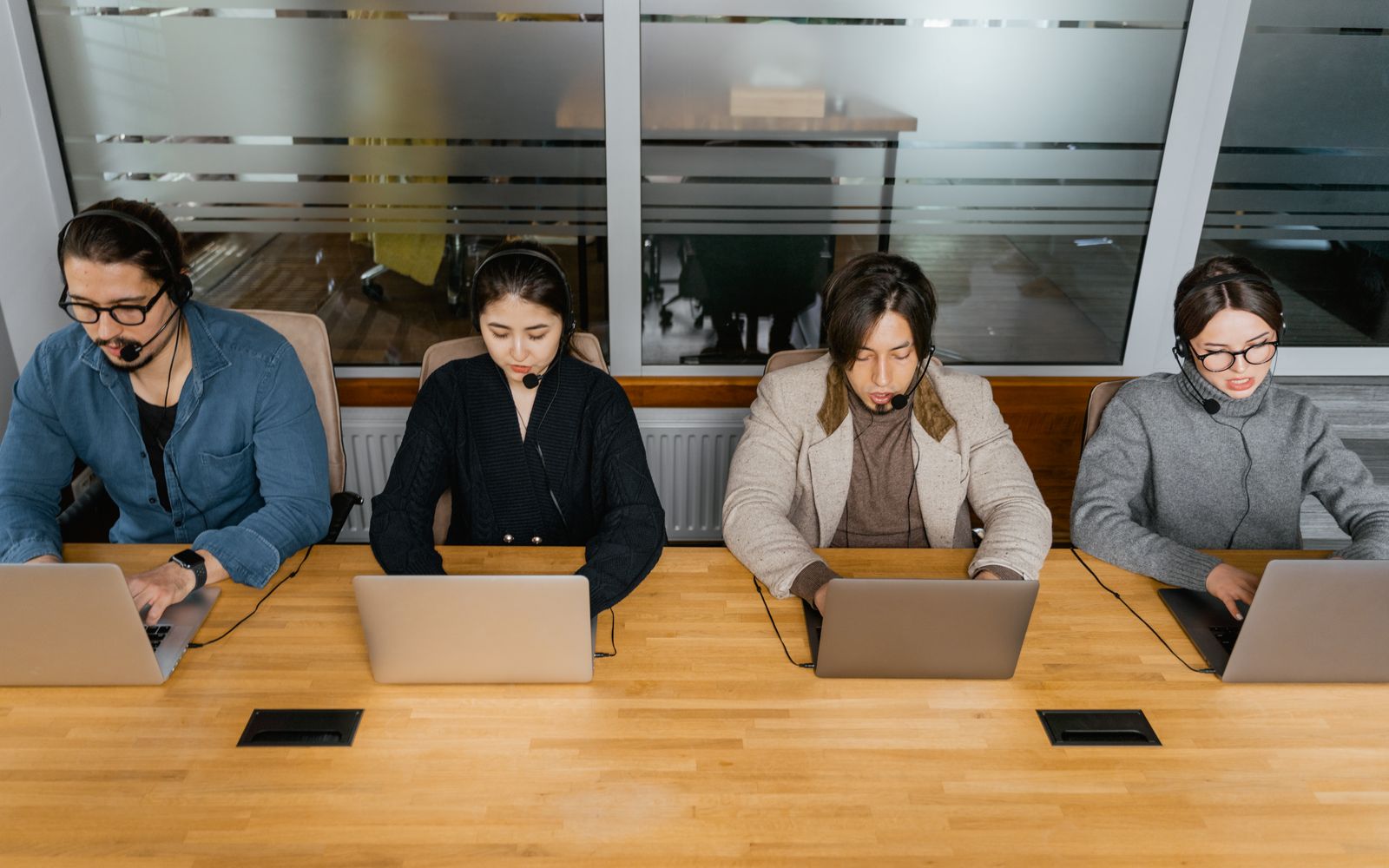Grupo de funcionários diversos usando fones de ouvido trabalhando em laptops em um ambiente de escritório moderno