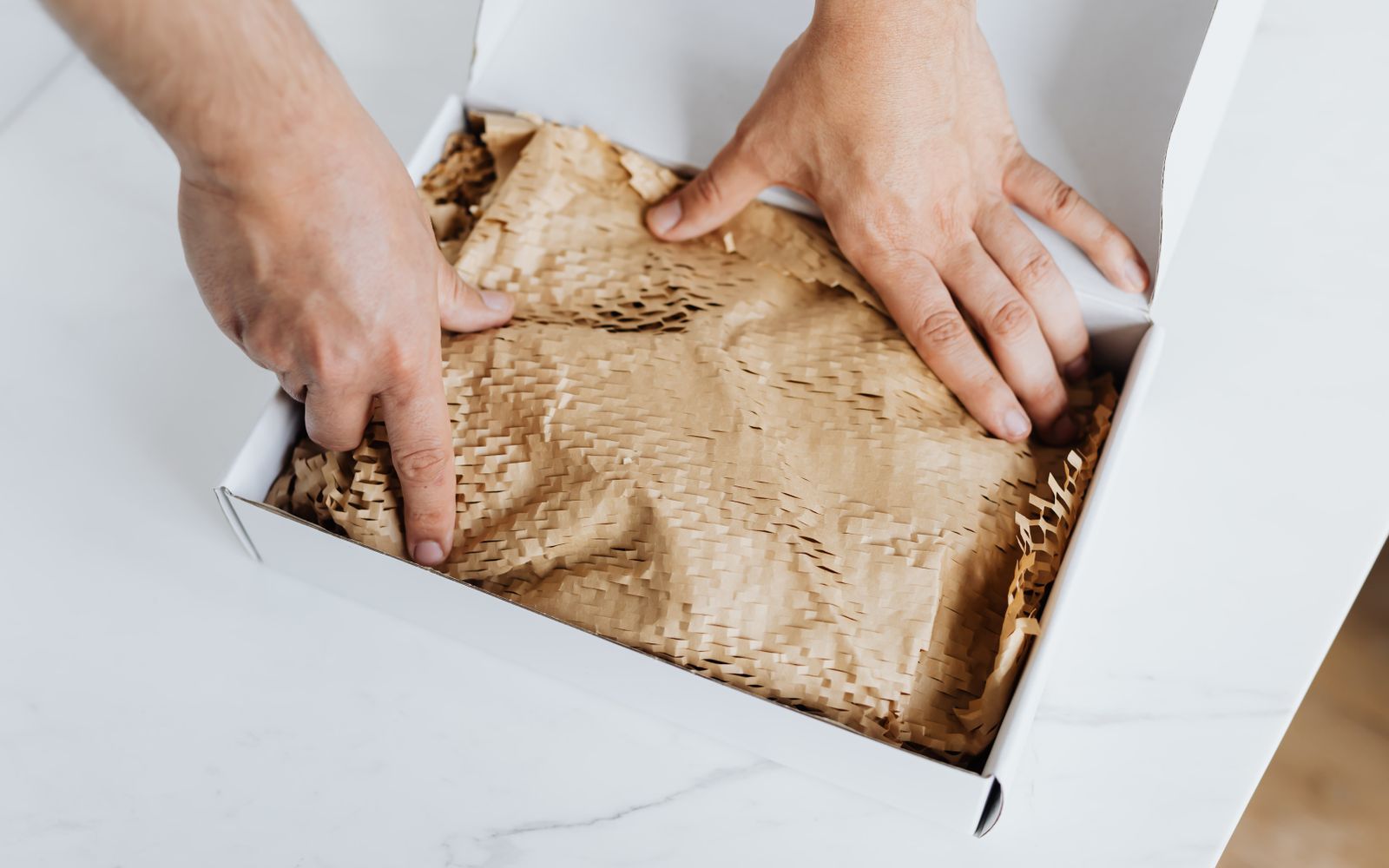 Homem embalando um produto em caixa branca com papel de proteção para envio