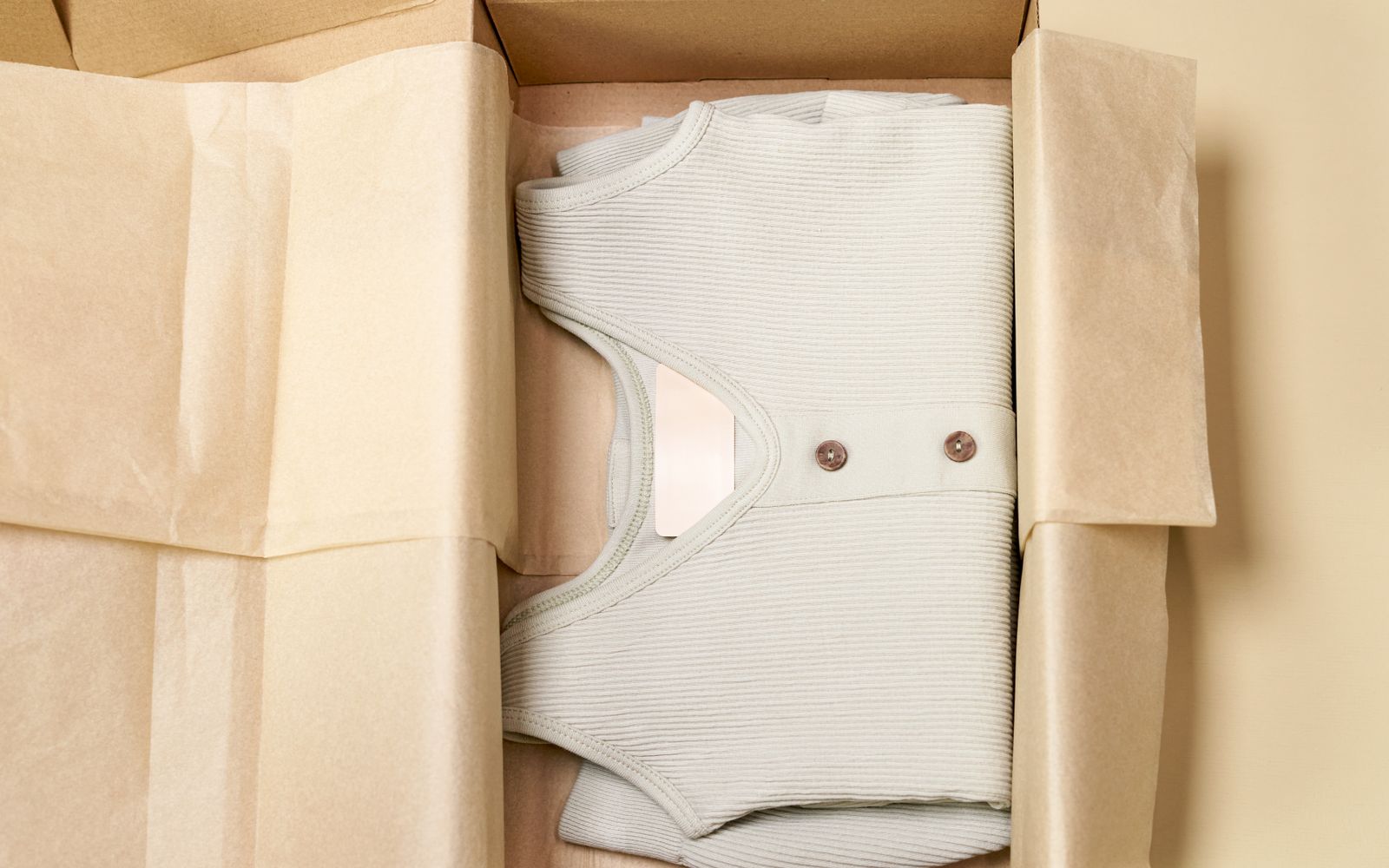 Peça de roupa bege dobrada dentro de uma caixa de papelão