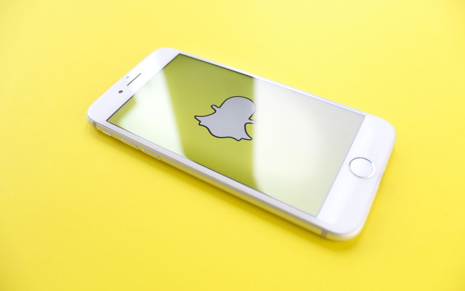 Celular branco exibindo o logo do Snapchat sobre fundo amarelo