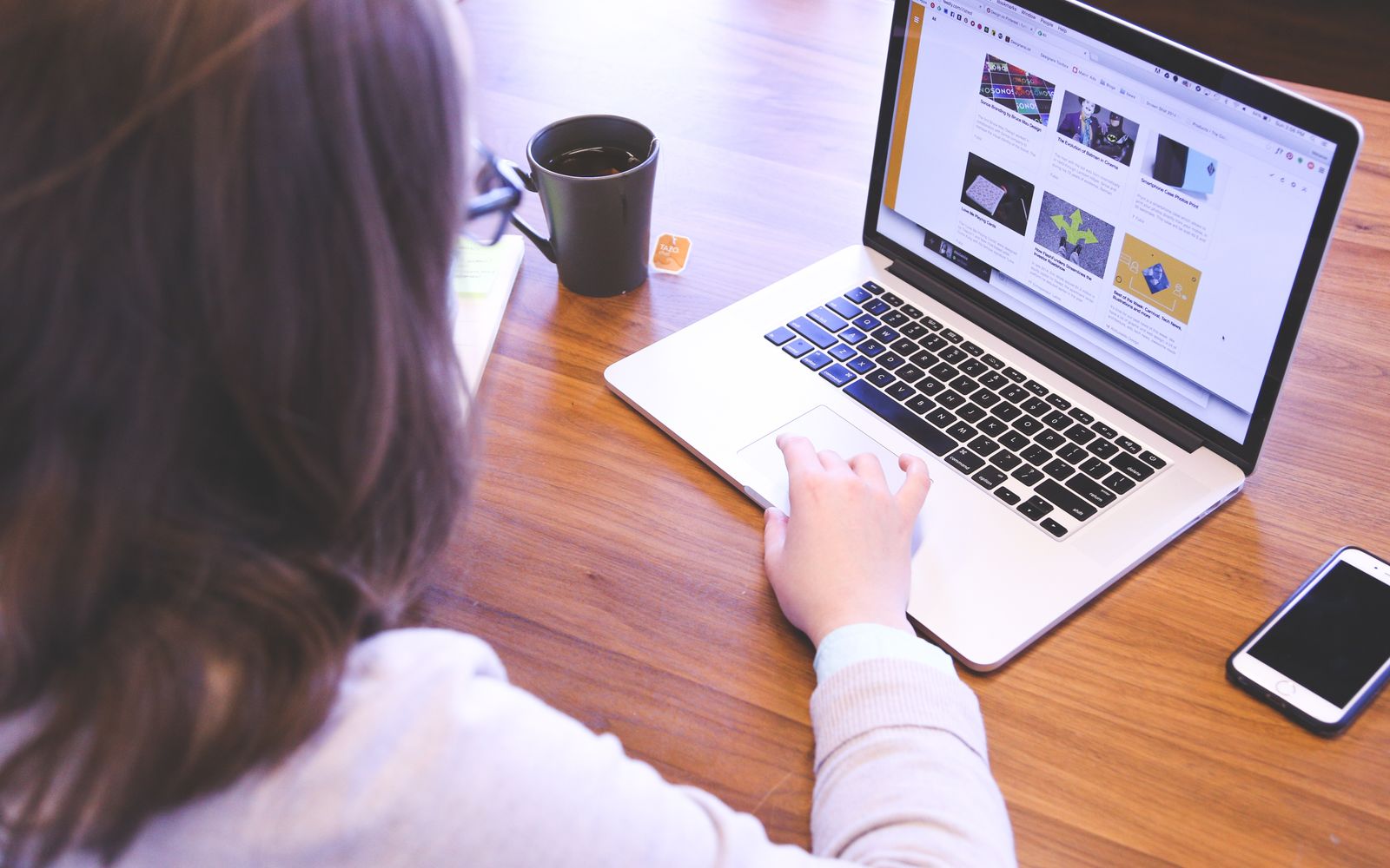 Pessoa navegando na internet em um MacBook, com celular ao lado