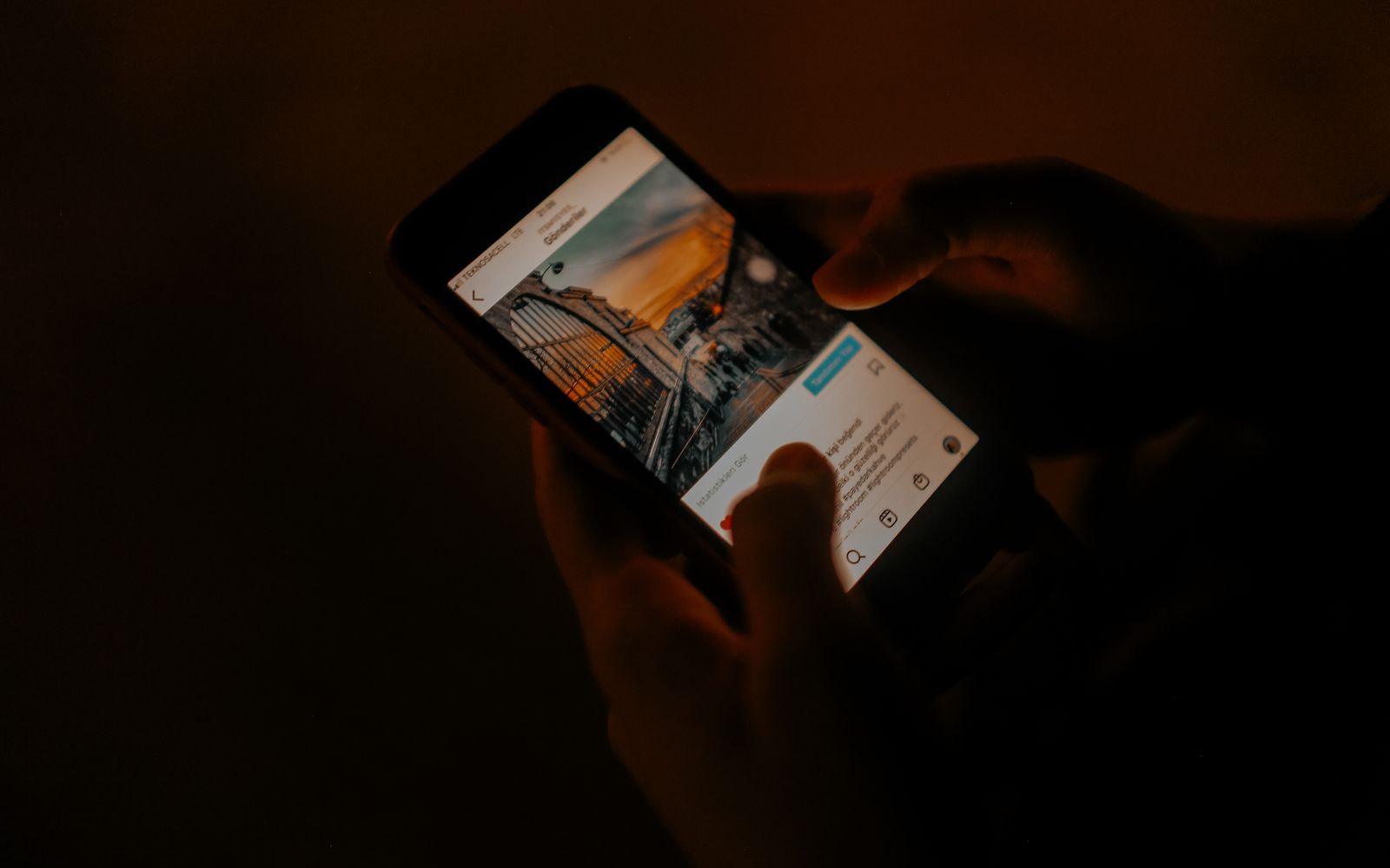Mãos segurando um celular nas redes sociais, em luz baixa