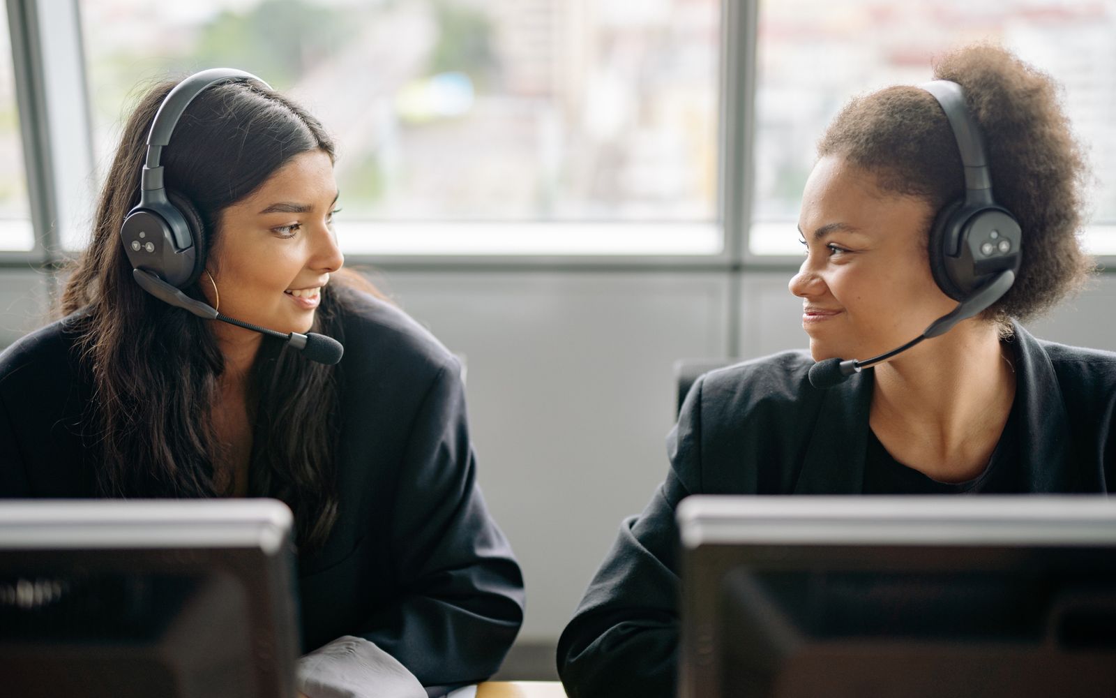 Duas atendentes sorrindo com headset, trabalhando juntas