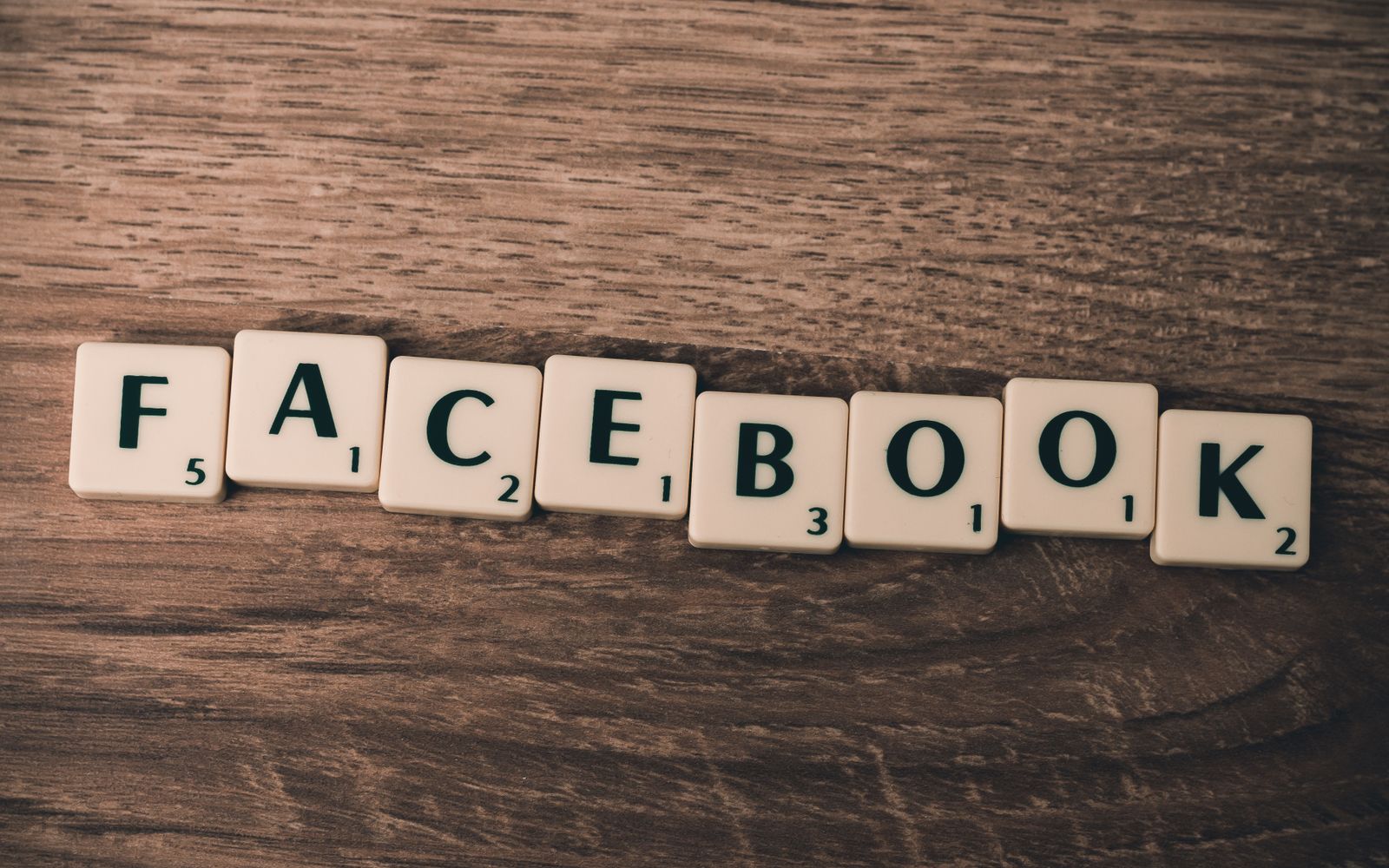 Peças de Scrabble formando a palavra 'Facebook' em fundo de madeira