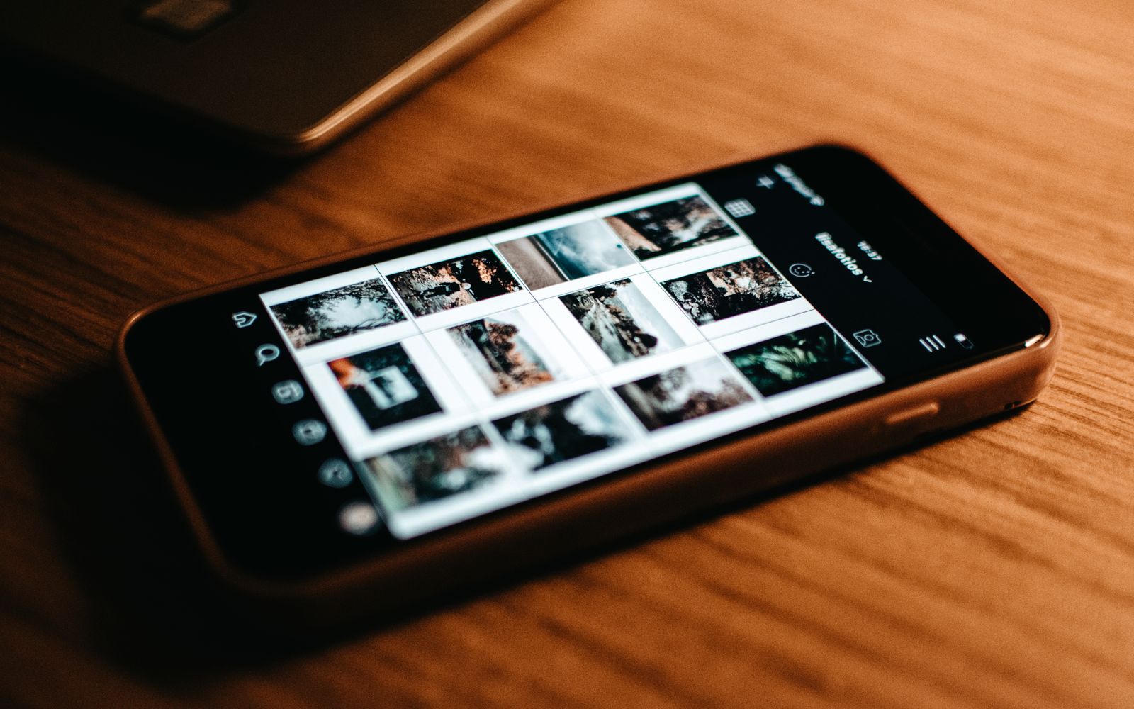 Foto em close-up de um smartphone mostrando a galeria de fotos em uma mesa de madeira