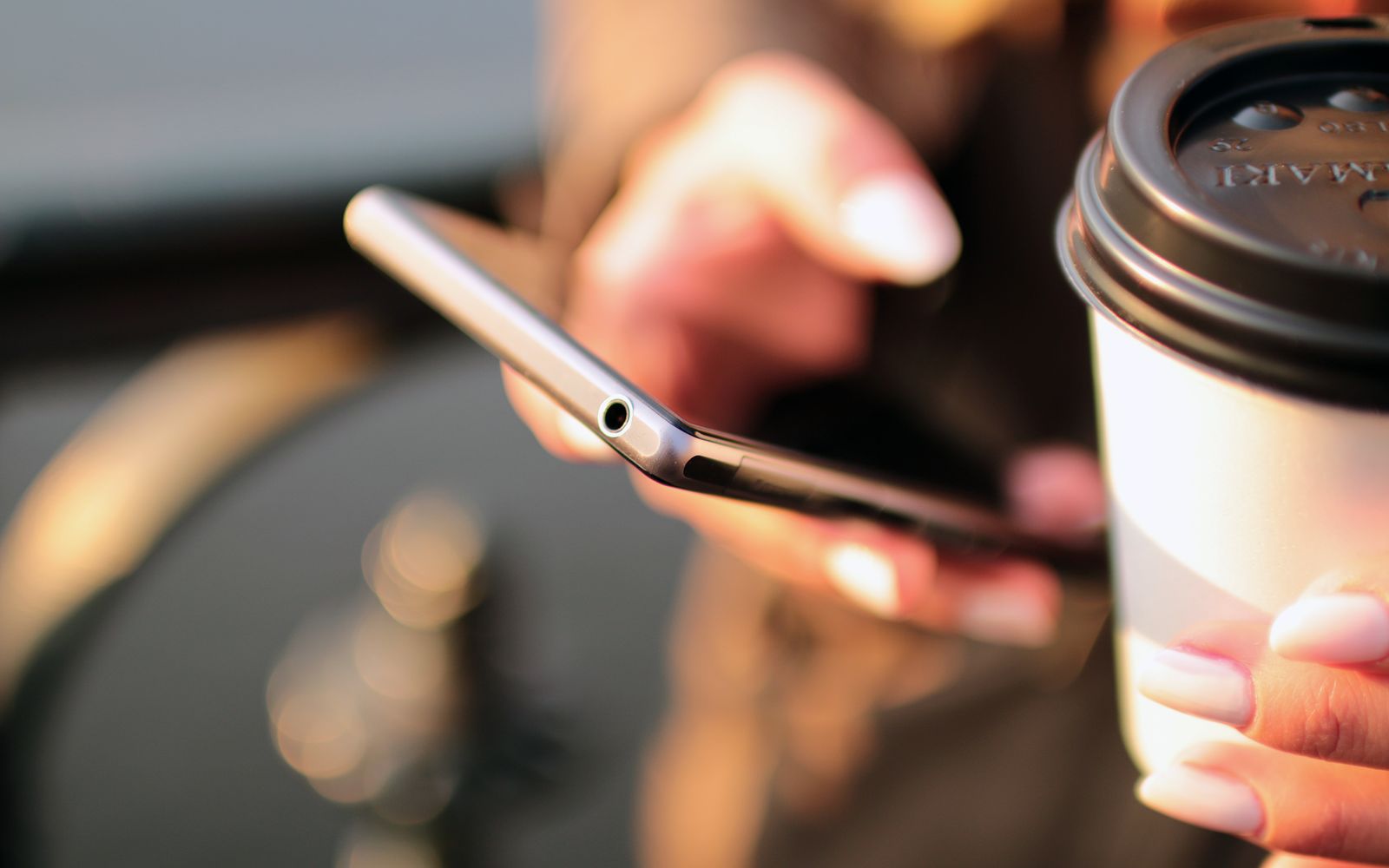 Pessoa digitando no celular com um copo de café na mão, na rua