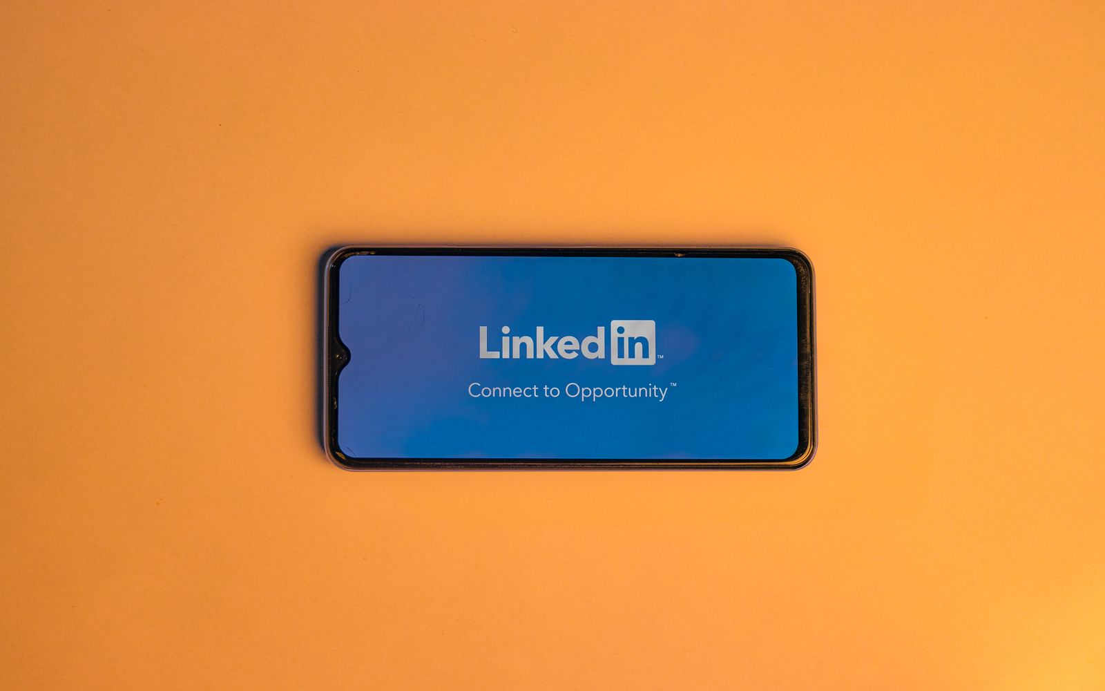 Celular com a tela de login do LinkedIn sobre fundo laranja