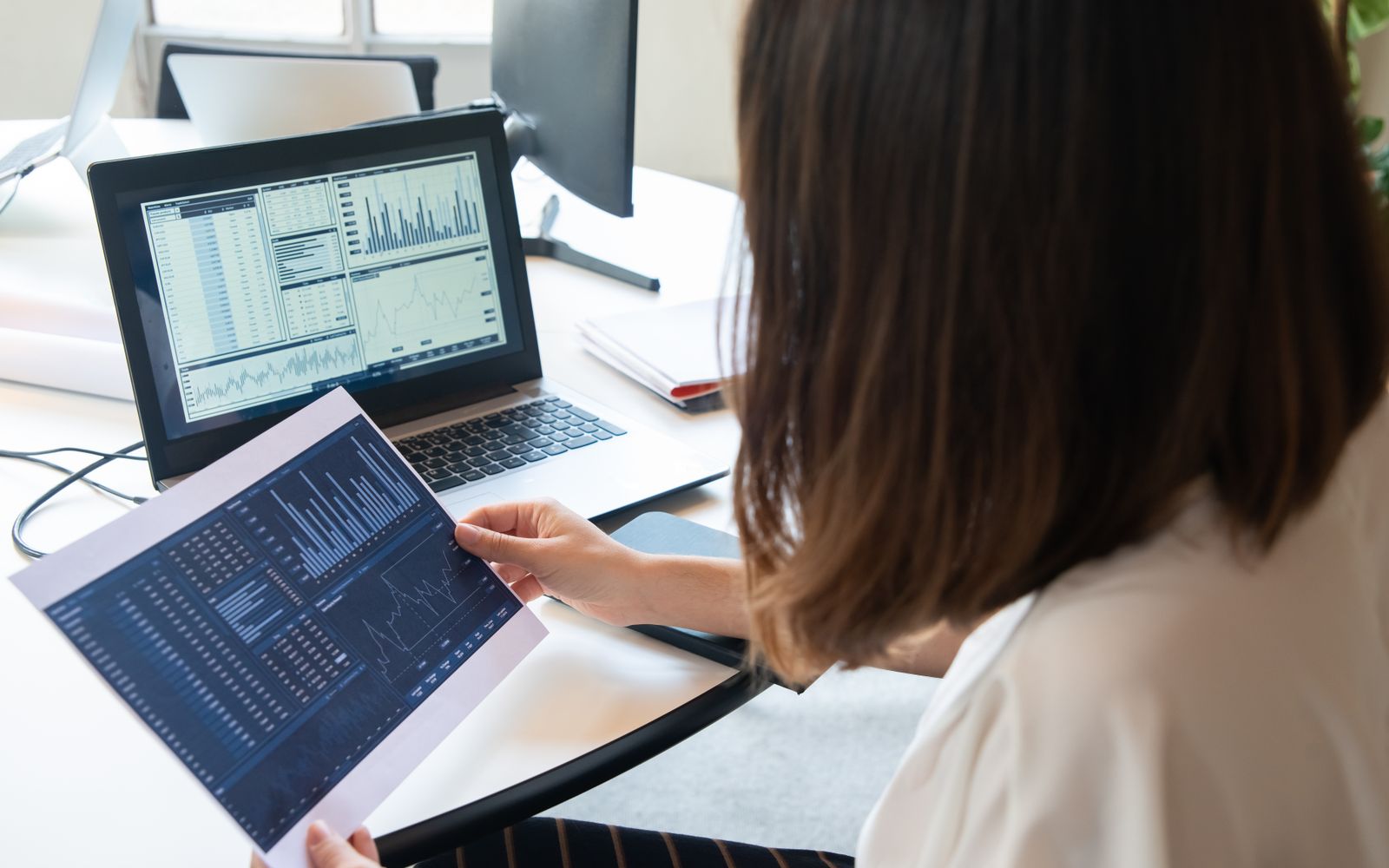 Uma mulher profissional analisa gráficos financeiros em um laptop e em papel para obter insights empresariais