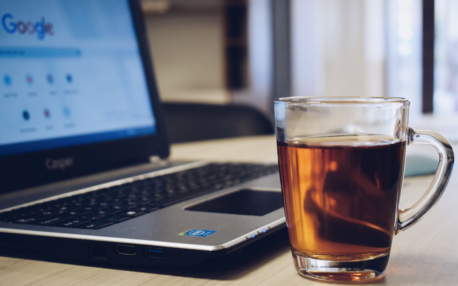 Mesa de madeira com notebook e um copo de chá quente