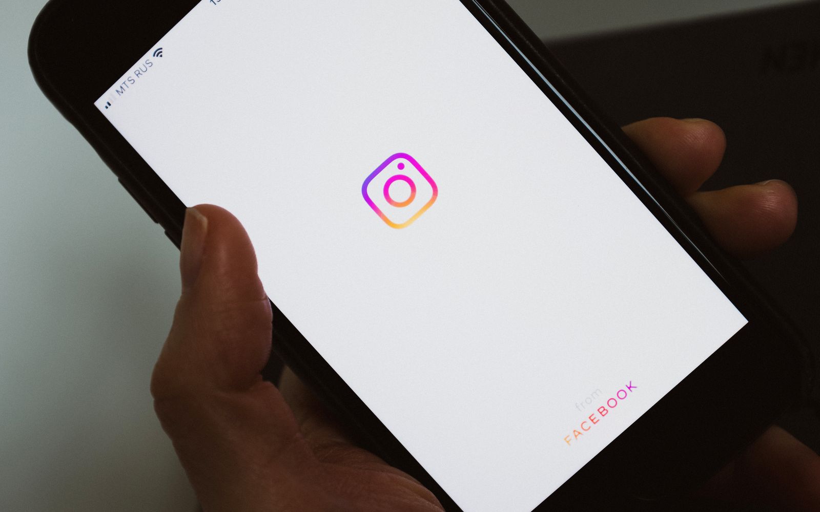 Pessoa segurando celular com a tela em branco e o logo de uma rede social