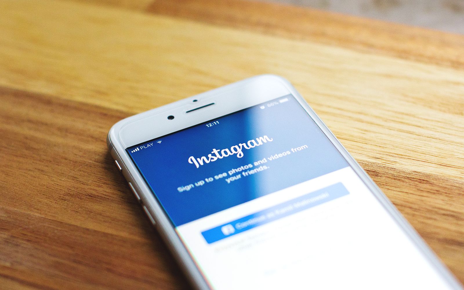 Foto em close-up de um smartphone mostrando o login do Instagram sobre uma mesa de madeira