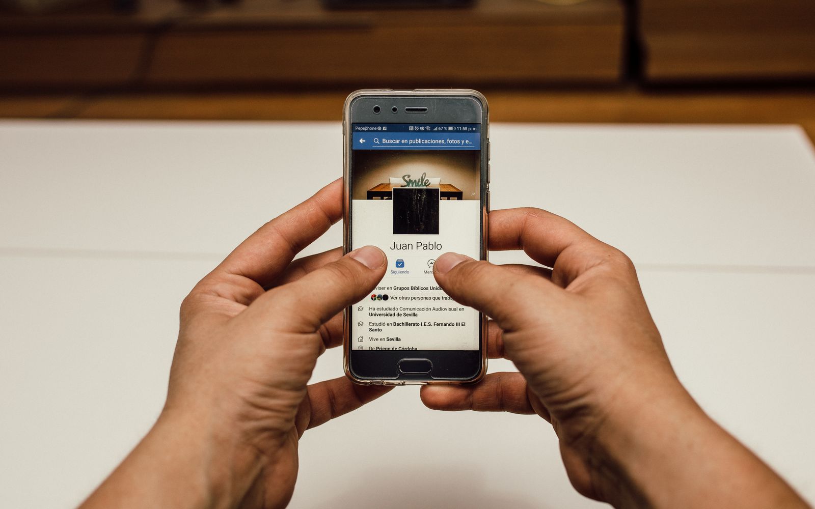 Foto em close de mãos usando um smartphone com uma página de redes sociais em ambiente interno