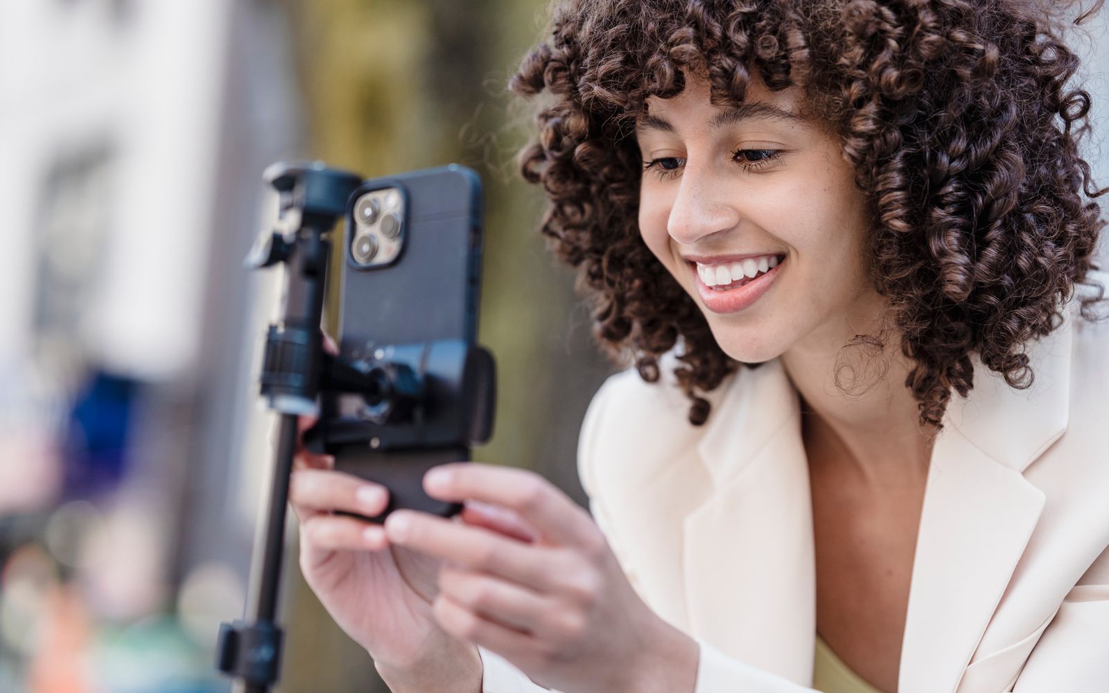 Mulher de cabelo cacheado gravando com celular em tripé ao ar livre